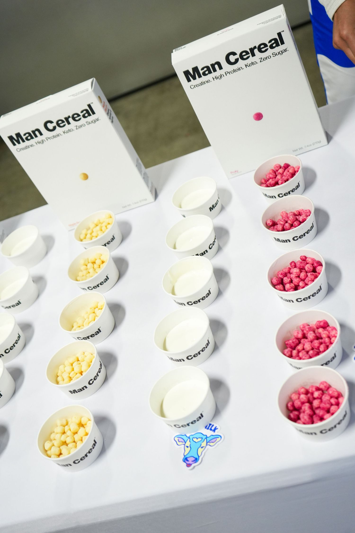 White bowls containing colorful cereal arranged in rows on a white surface with text-labeled packaging visible.