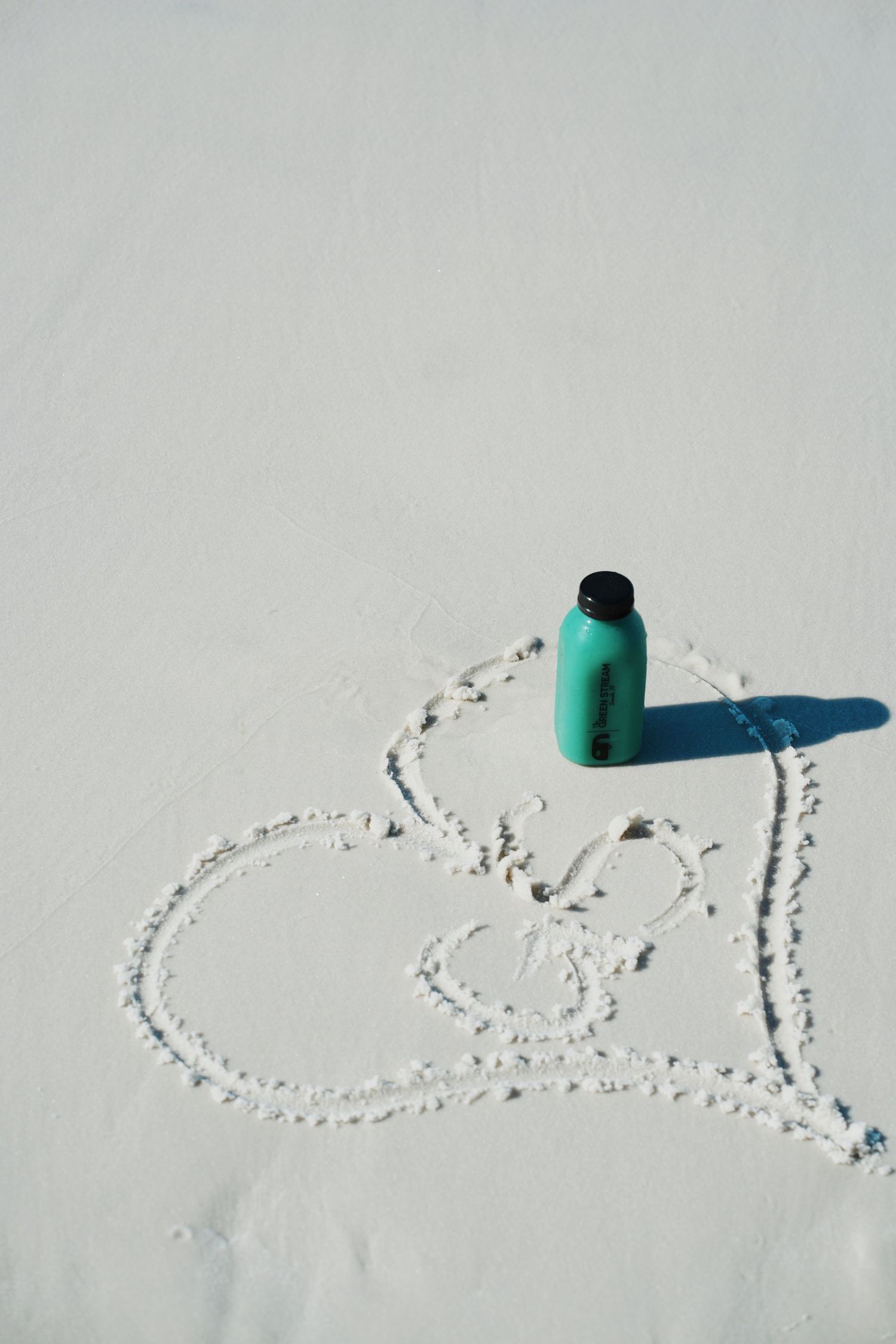 Someone writes a message in the snow using a green water bottle as a marking tool creating curved lines.
