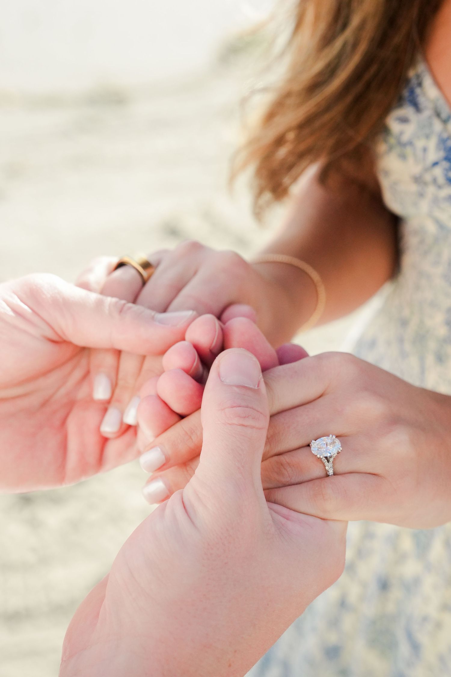 Close-up of couple holding hands outdoors, woman wearing a stunning diamond engagement ring with halo setting.