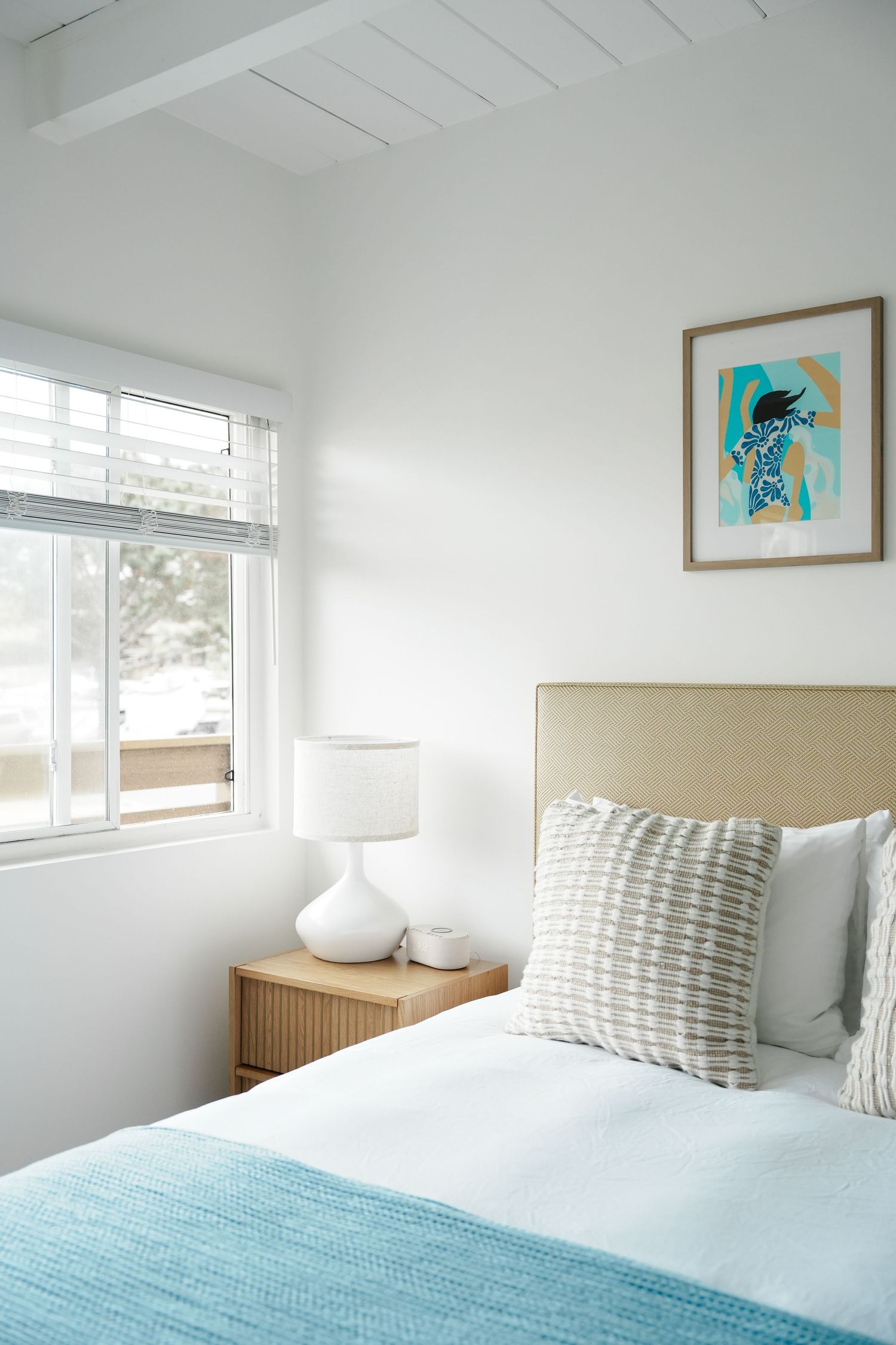 Modern bedroom with turquoise bedding, white walls, and natural light streaming through windows.