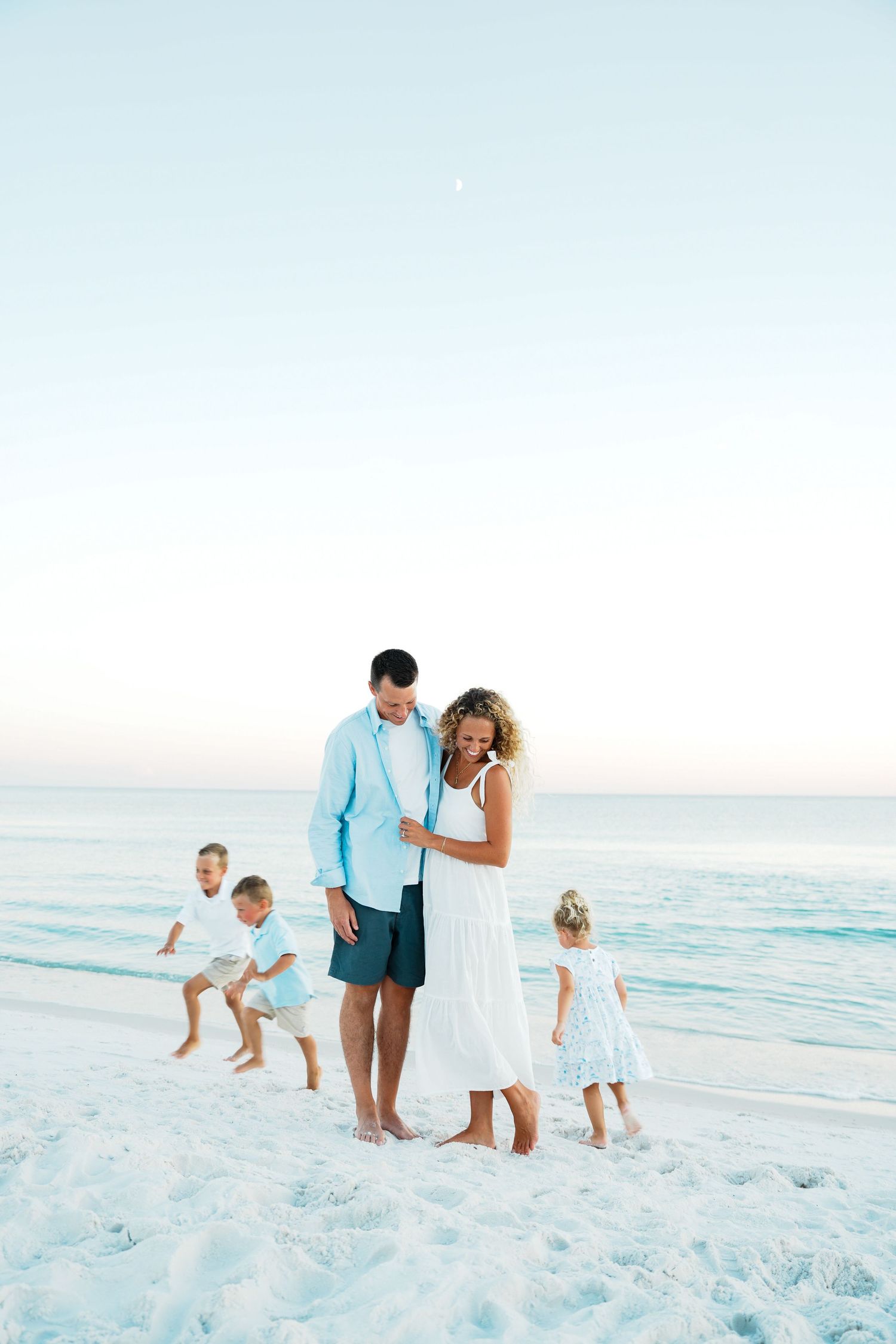 Family enjoying a peaceful moment together walking along a white sandy beach at sunset with gentle waves in the background.