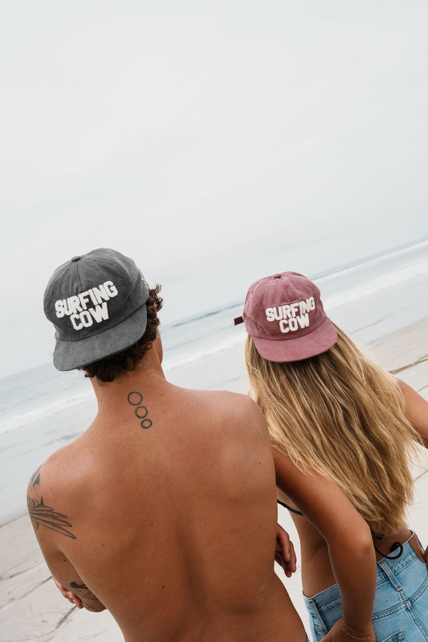 Three people wearing surfing caps sitting on beach looking at ocean.