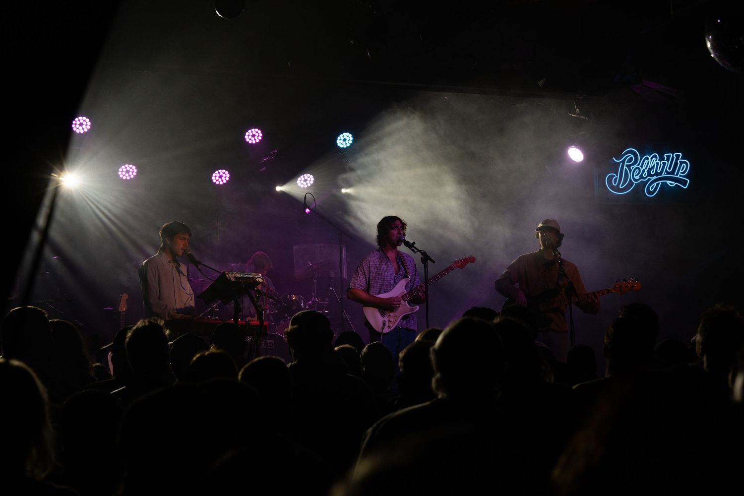 Concert performers silhouetted on stage with atmospheric purple and blue lighting effects during a live music performance.