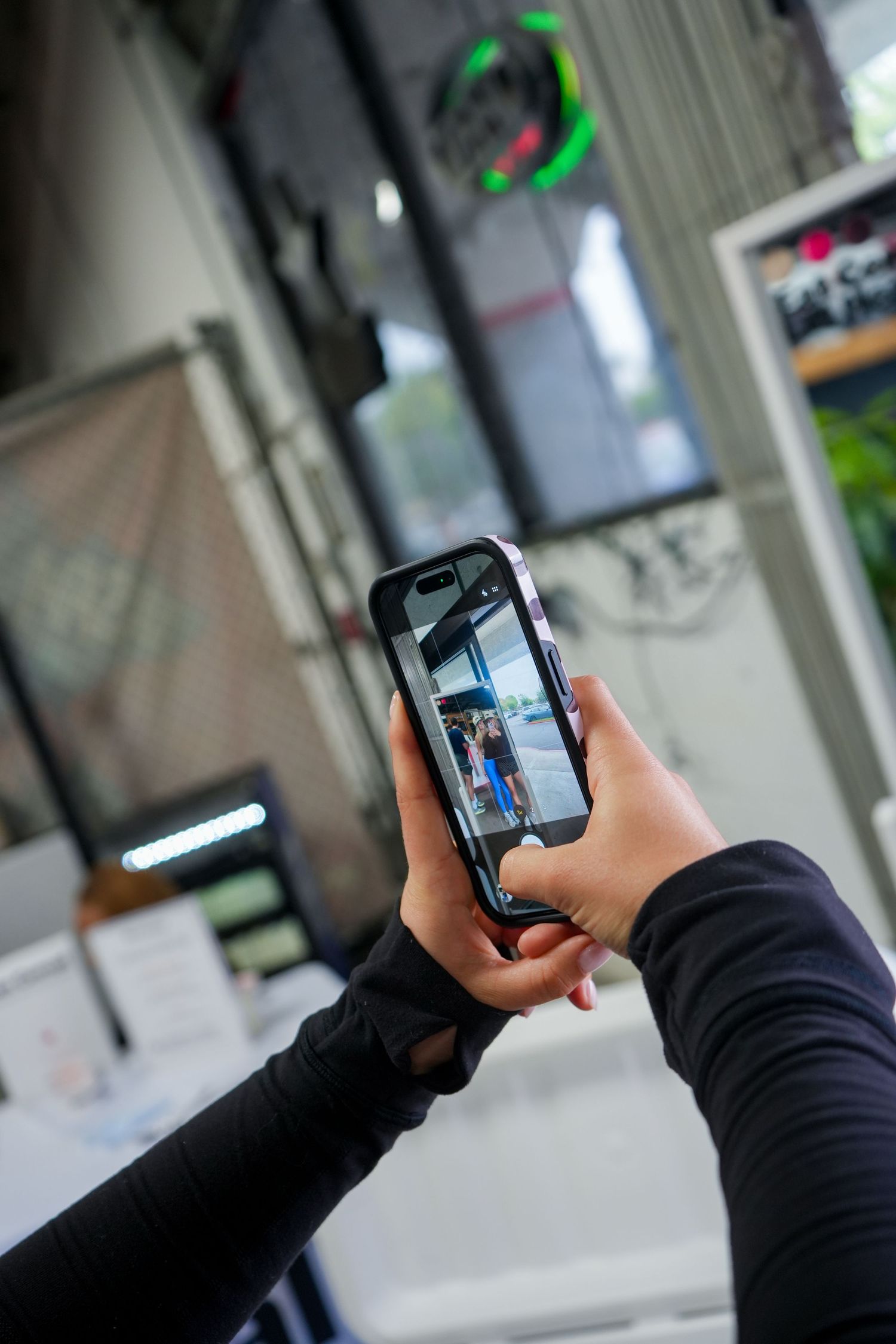 Hand holding smartphone to take photos in indoor setting with green lighting visible.