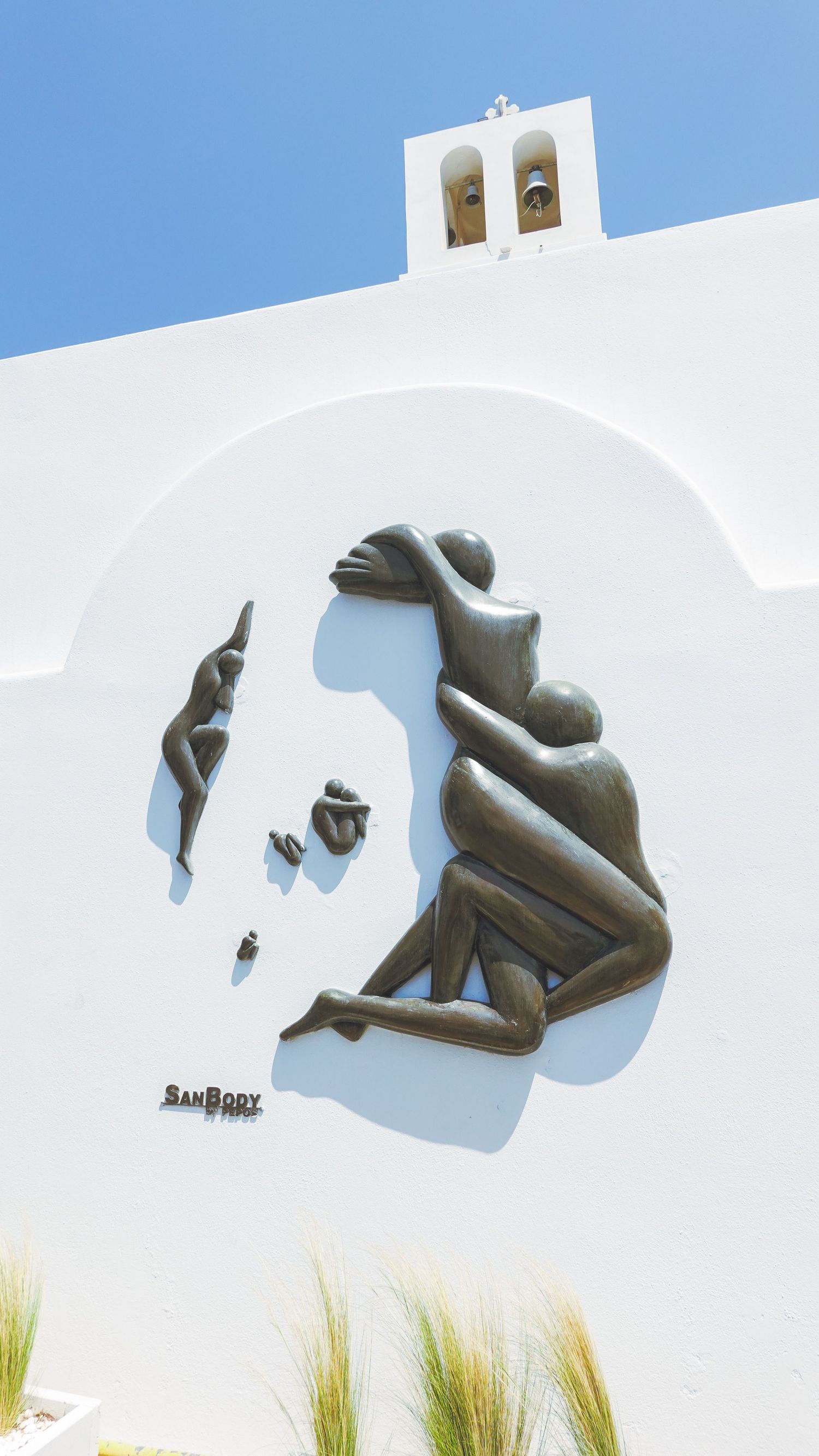 White church wall with artistic cutout silhouette design and bell tower in Greece.