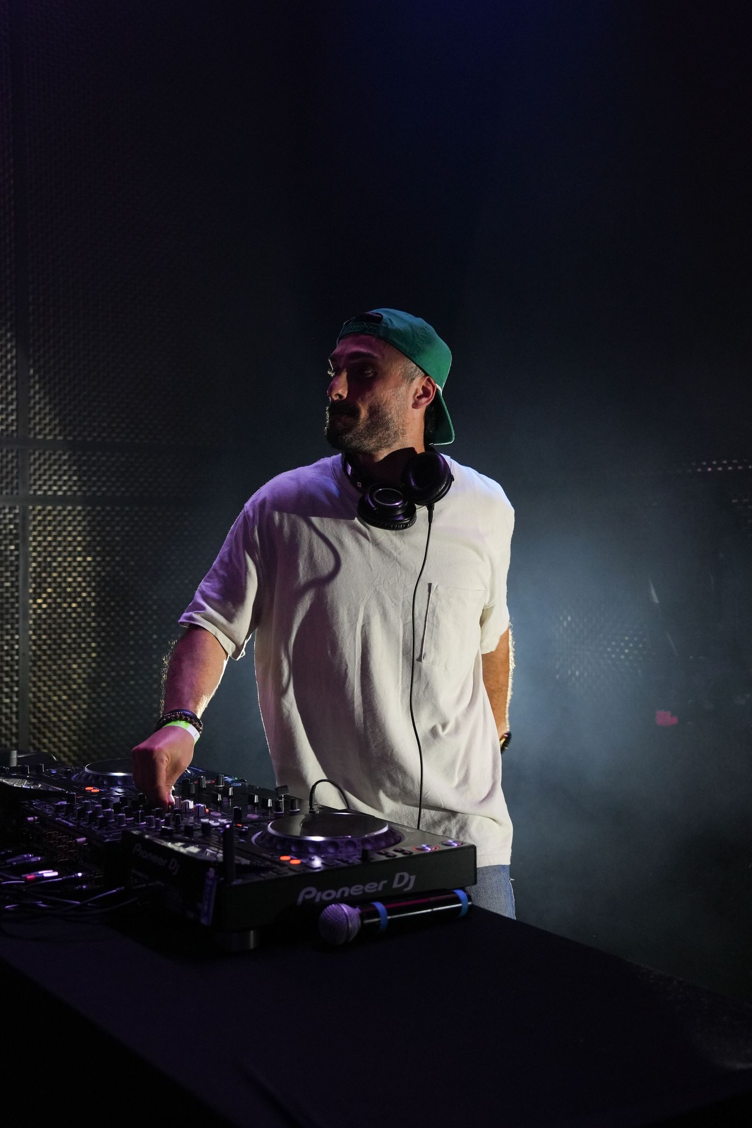 DJ performs on stage with turntables and mixer equipment in dark atmospheric lighting during nightclub performance.