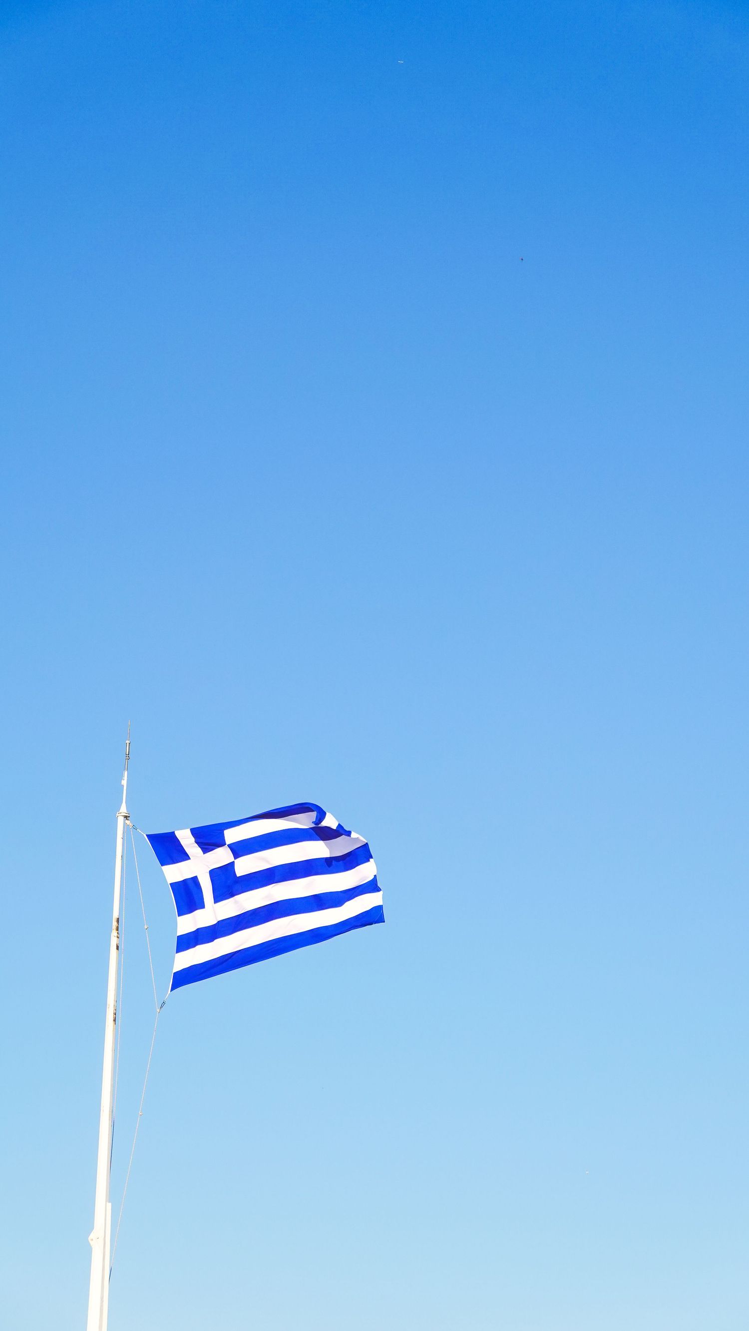 Greek flag waving against a vivid blue sky on a flagpole.