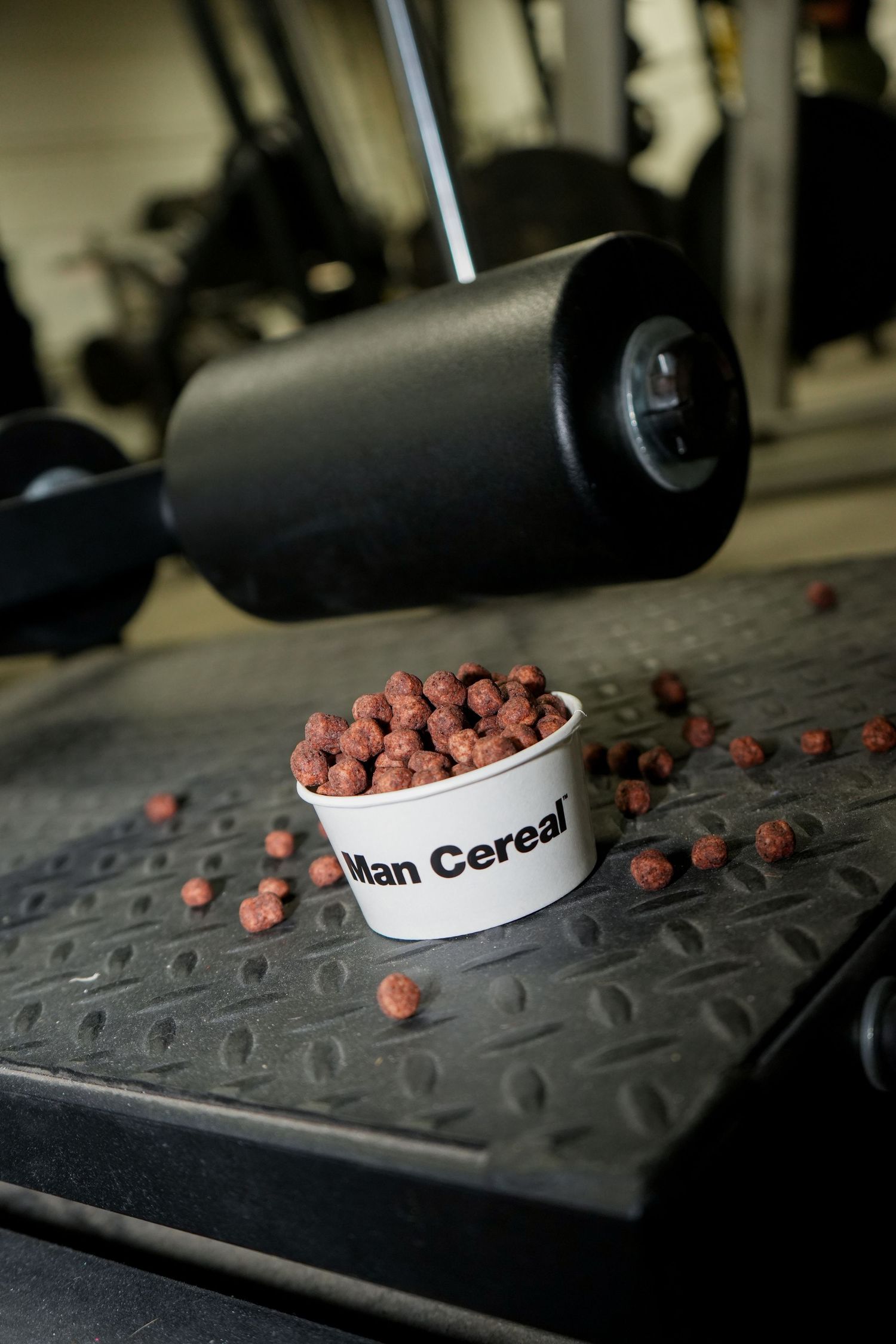 Small chocolate cereal balls scattered across a dark textured surface with a white bowl in view.