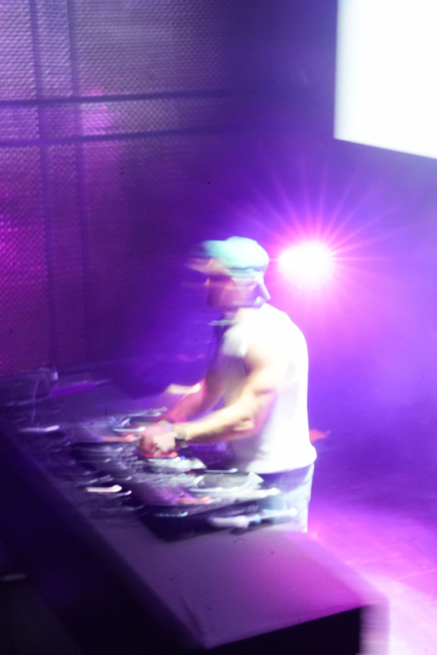 DJ performs at a nightclub with purple lighting and bright flare effects while mixing music at the turntables.