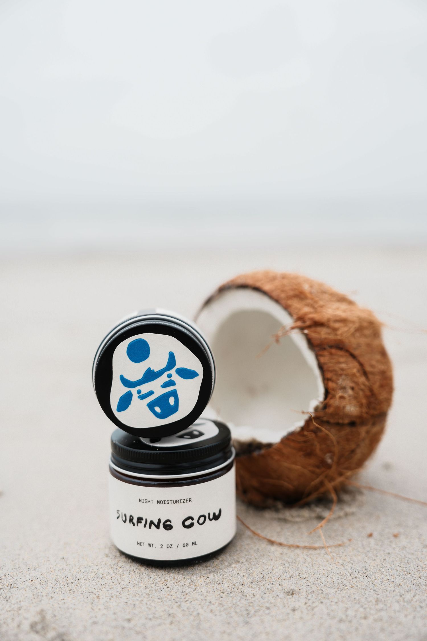 Surfing sunscreen product containers arranged with coconuts on sandy beach background.