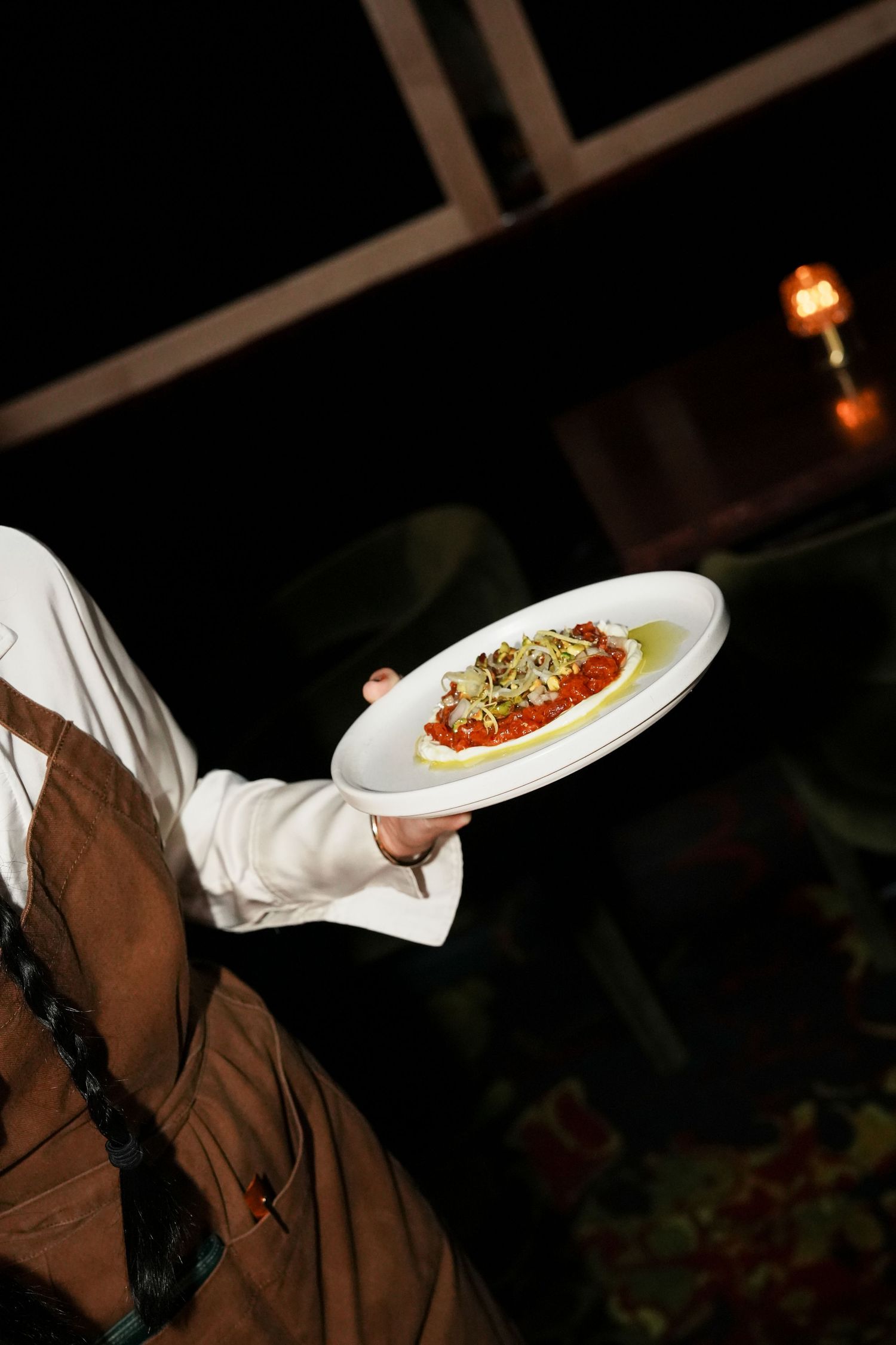 Waiter in brown apron presenting an elegant pasta dish with red sauce on a white plate at a restaurant.