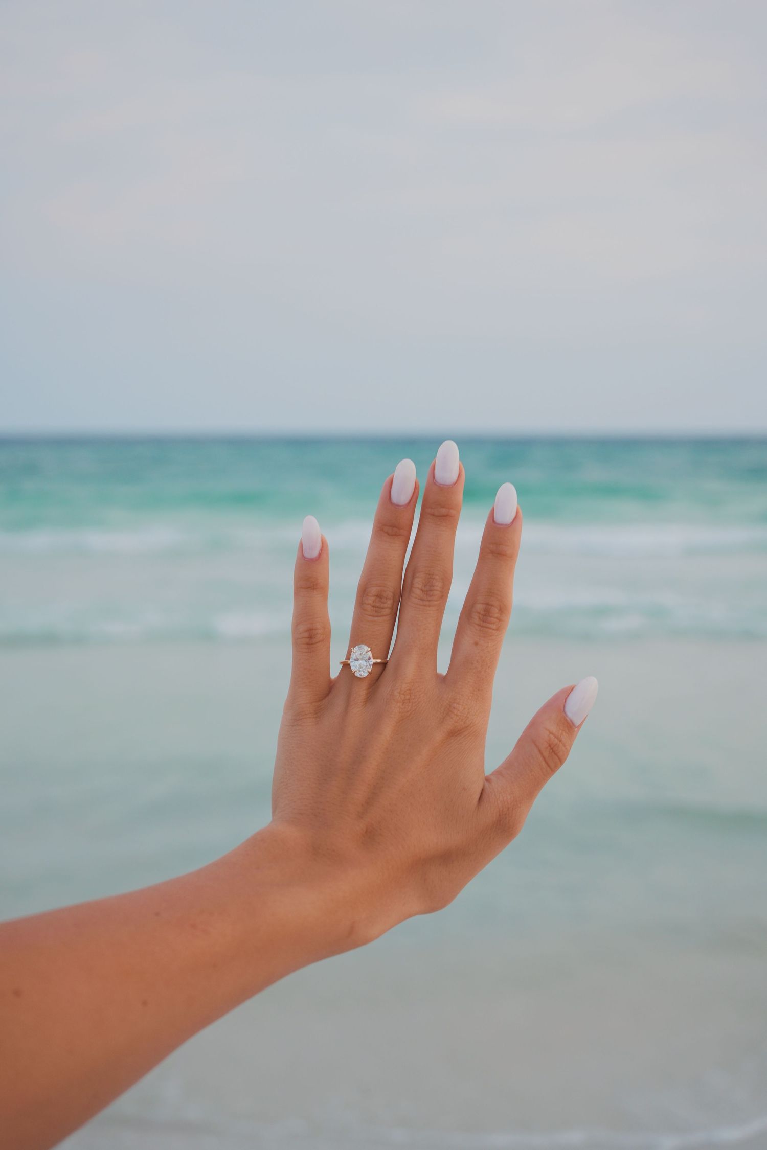 Woman's hand with engagement ring shown against turquoise ocean backdrop in multiple poses.