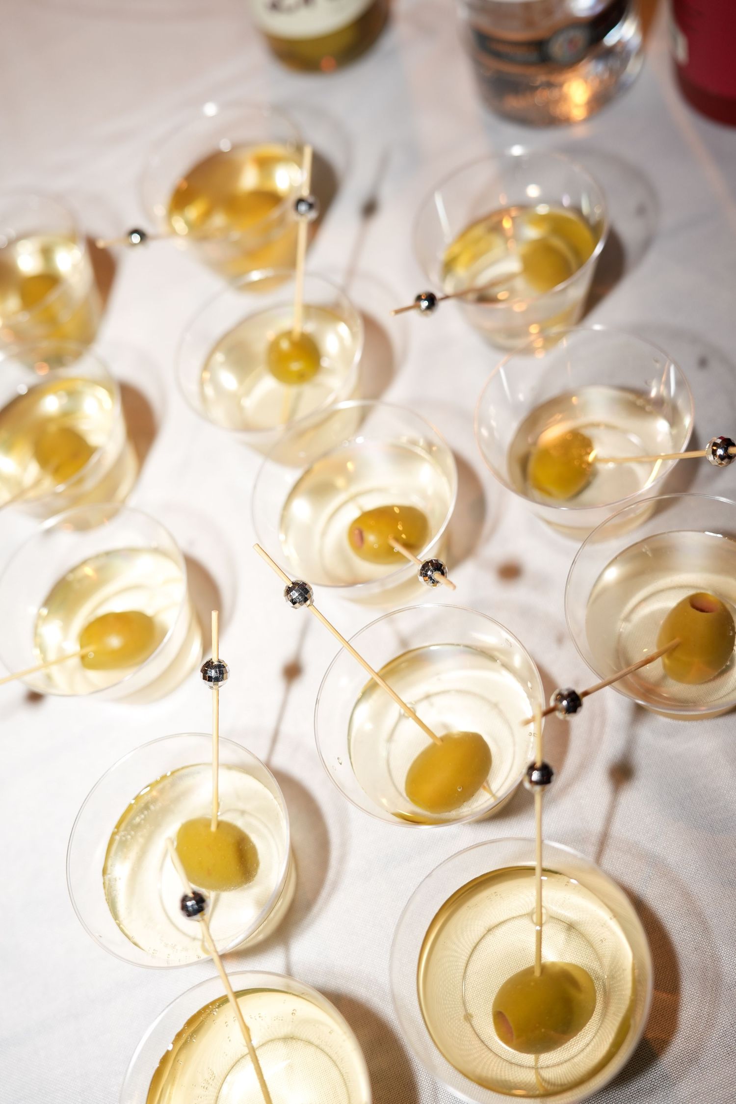 Rows of martini glasses filled with clear cocktails garnished with olives on skewers arranged on a white tablecloth.