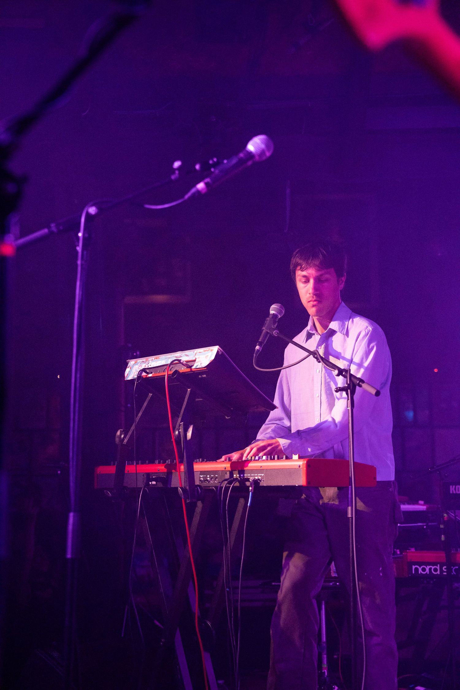 A musician performs on stage with electronic equipment in a dark purple-lit concert venue.