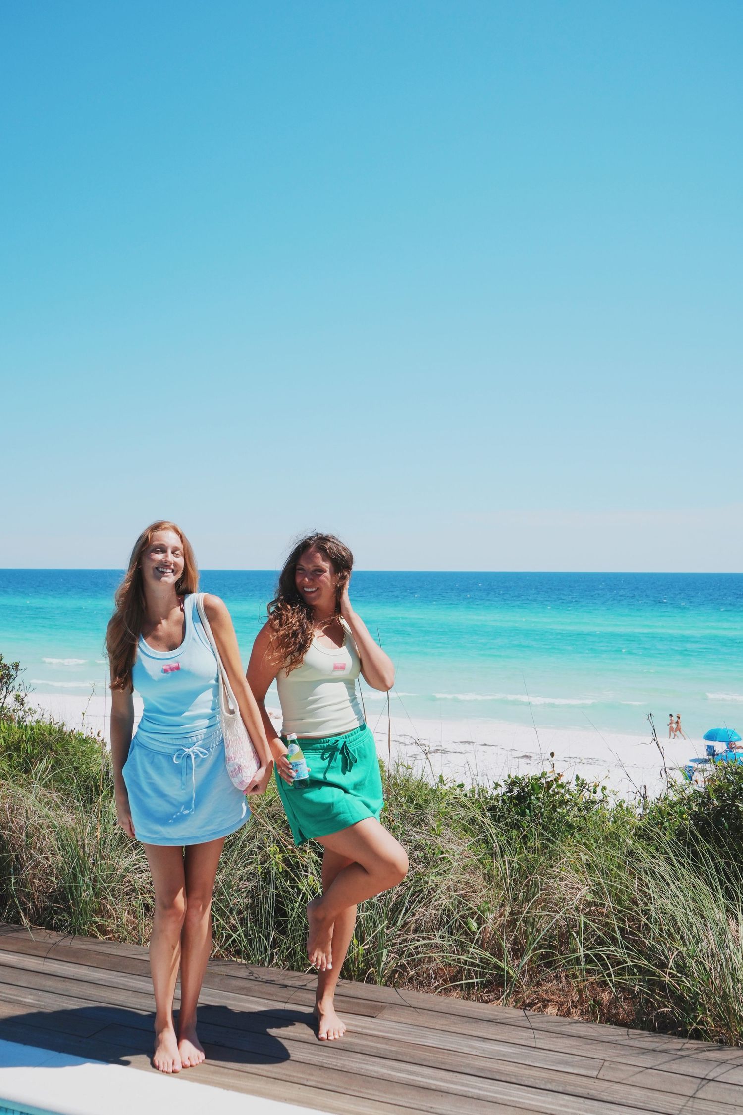 Beach friends in coordinating dresses enjoying a sunny day on a wooden boardwalk by turquoise ocean.