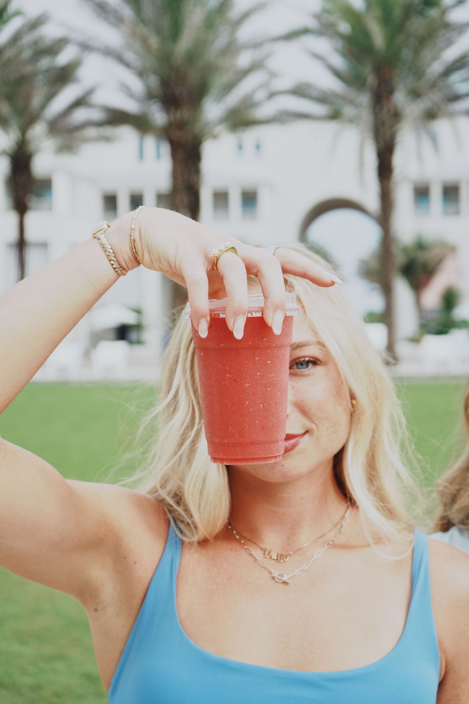 Four similar photos showing someone in a blue tank top holding a pink smoothie glass against tropical palm trees and greenery.