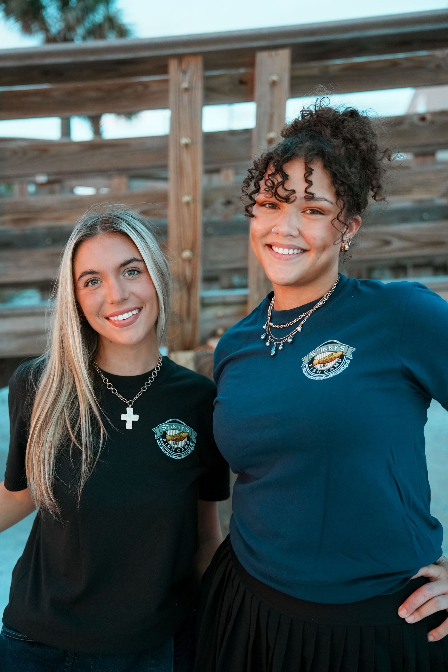 Two people wearing matching navy blue shirts with a logo smile while posing together outdoors.