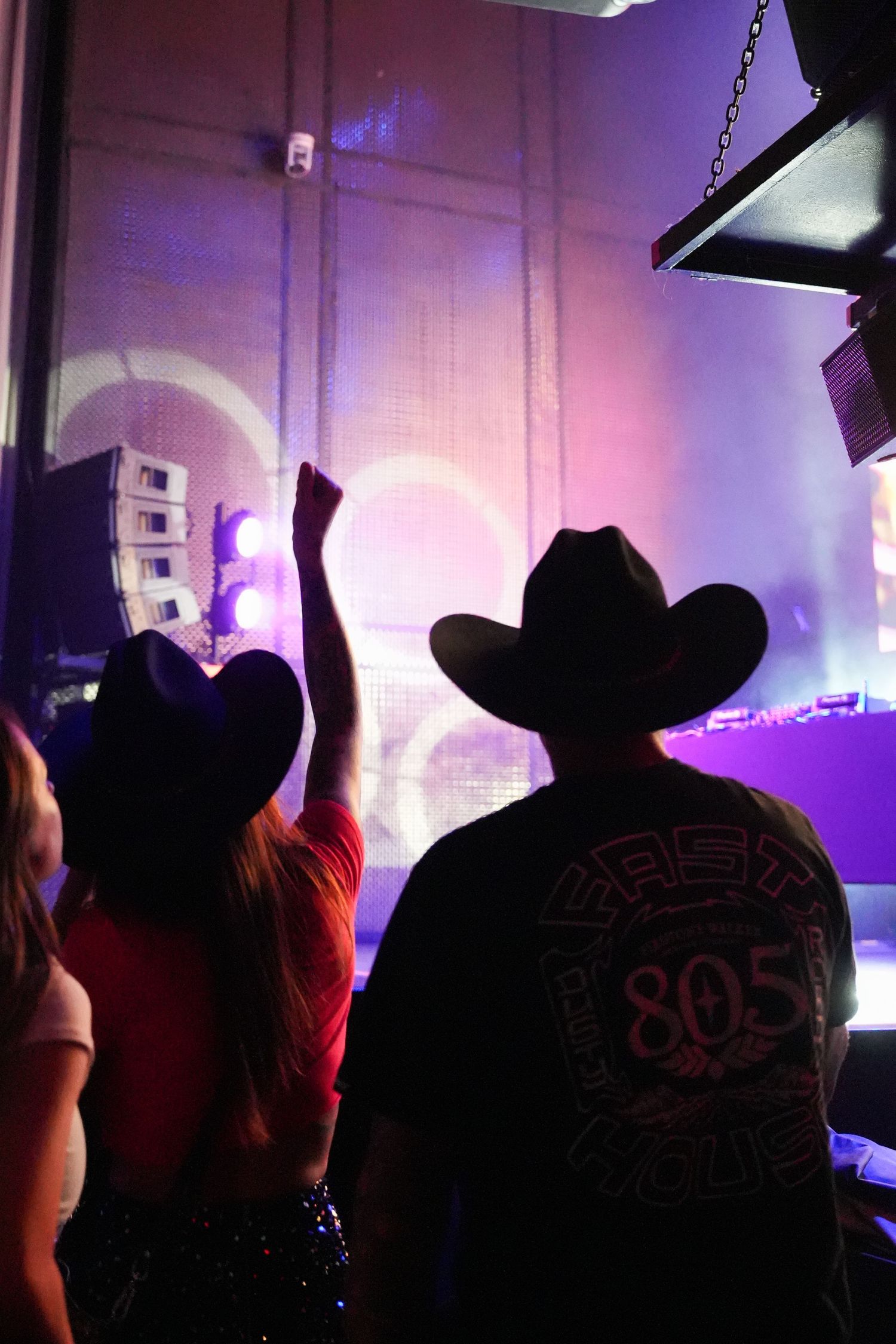 Silhouettes of people wearing Mickey Mouse ears against a purple-lit backdrop at a Disney event.