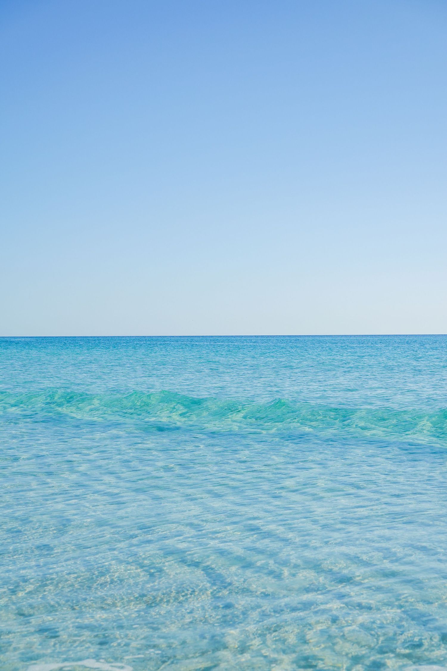 Crystal clear turquoise ocean water meeting bright blue sky at the horizon on a calm tropical day.