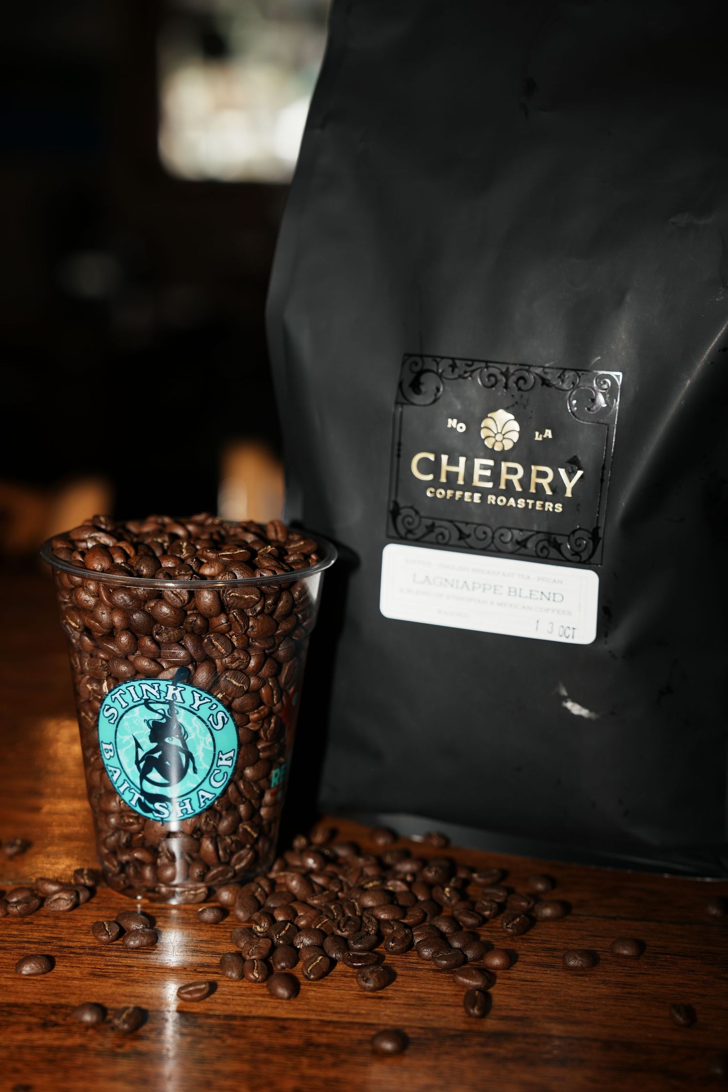 A bag of Cherry Coffee Roasters beans and branded cup filled with coffee beans on a dark wooden surface.
