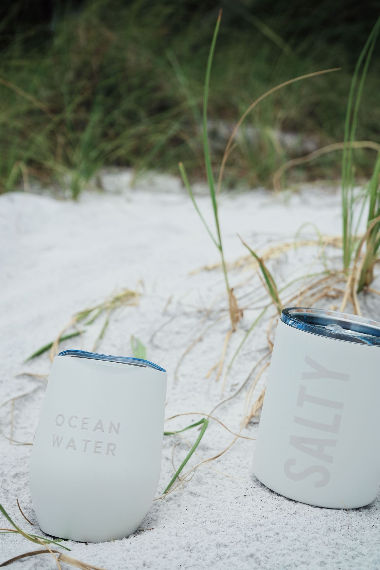 Row of clean white tins arranged in a line on sand with beach grass in the background.