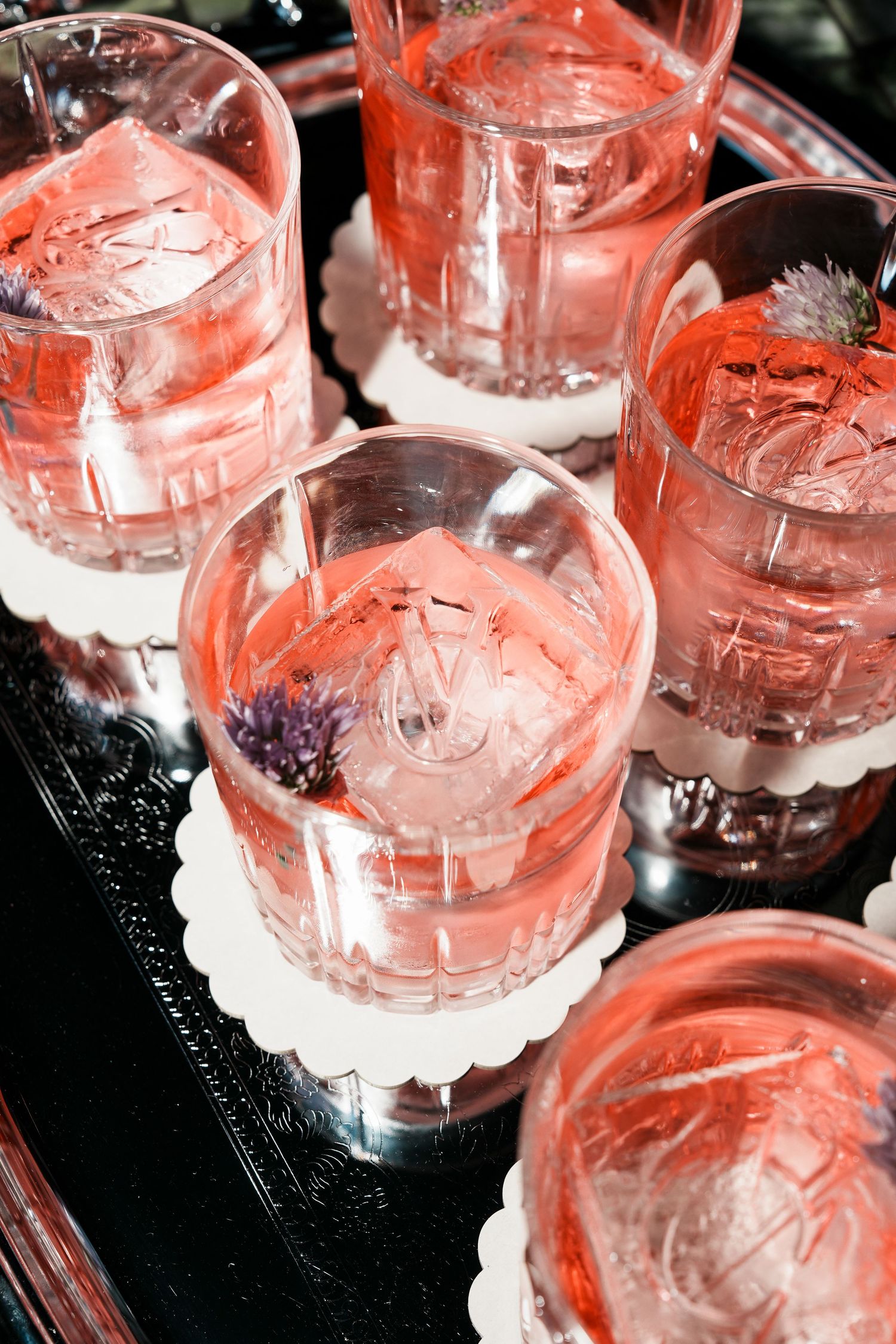 Crystal glasses filled with pink cocktails garnished with lavender flowers, served on a silver tray with white coasters.