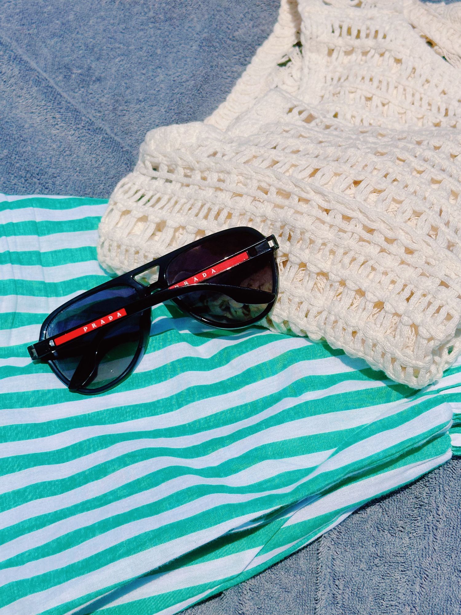 Black sunglasses and cream knit sweater arranged on green and white striped fabric.