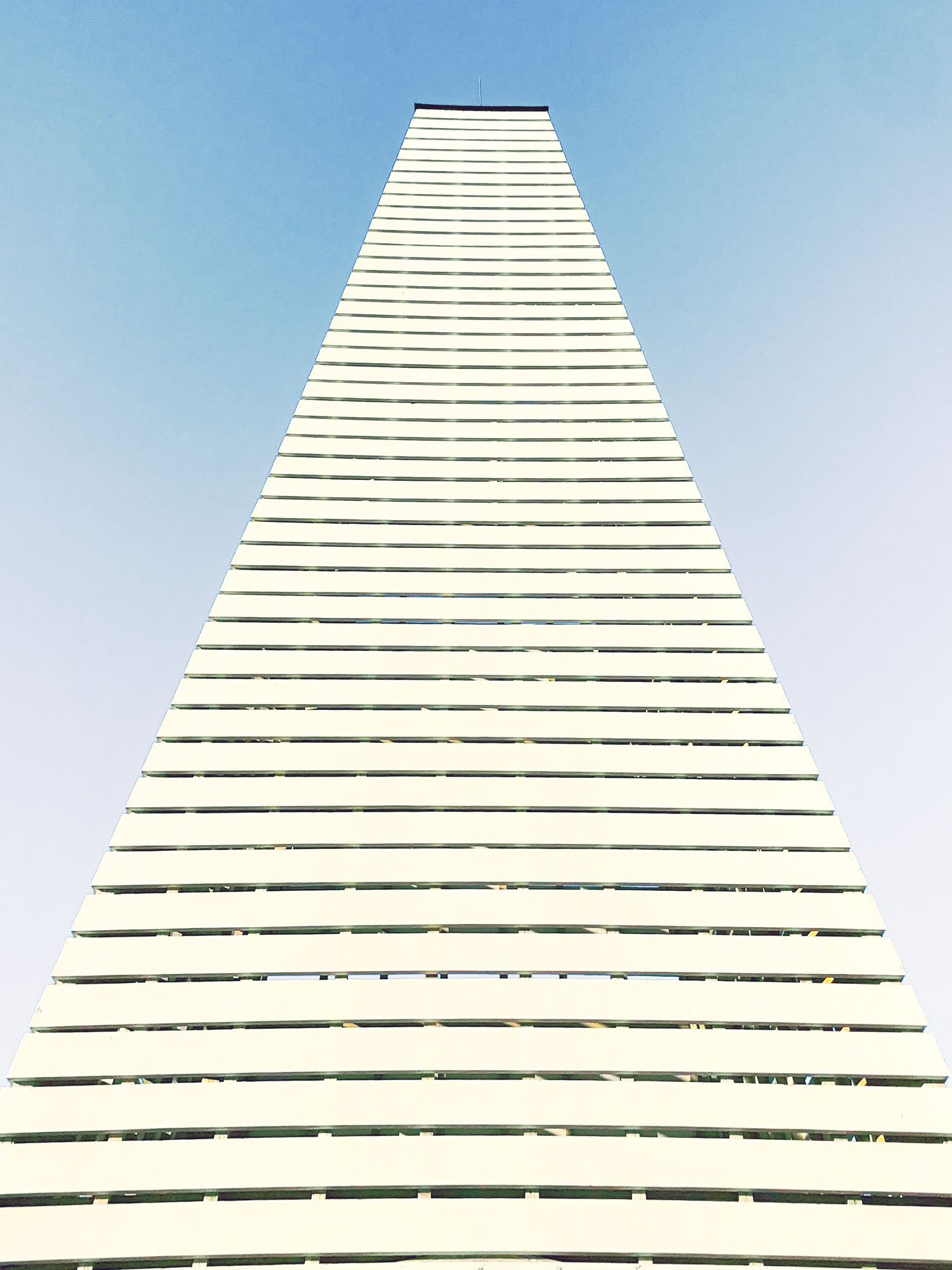 Looking up at a tall white architectural structure with horizontal lines against a blue sky.