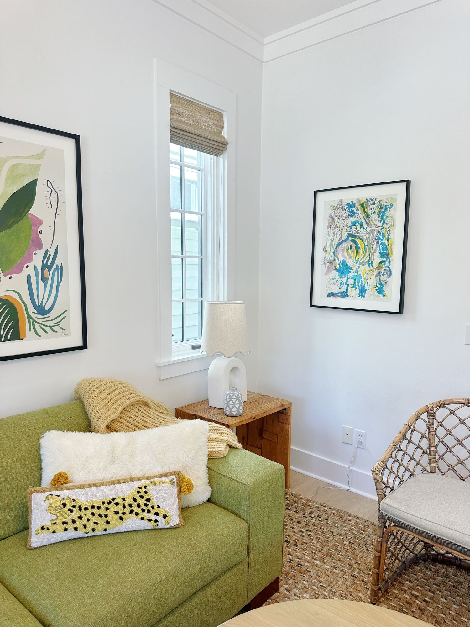 Cozy living room corner with green sofa, abstract art prints, and natural woven window shade.
