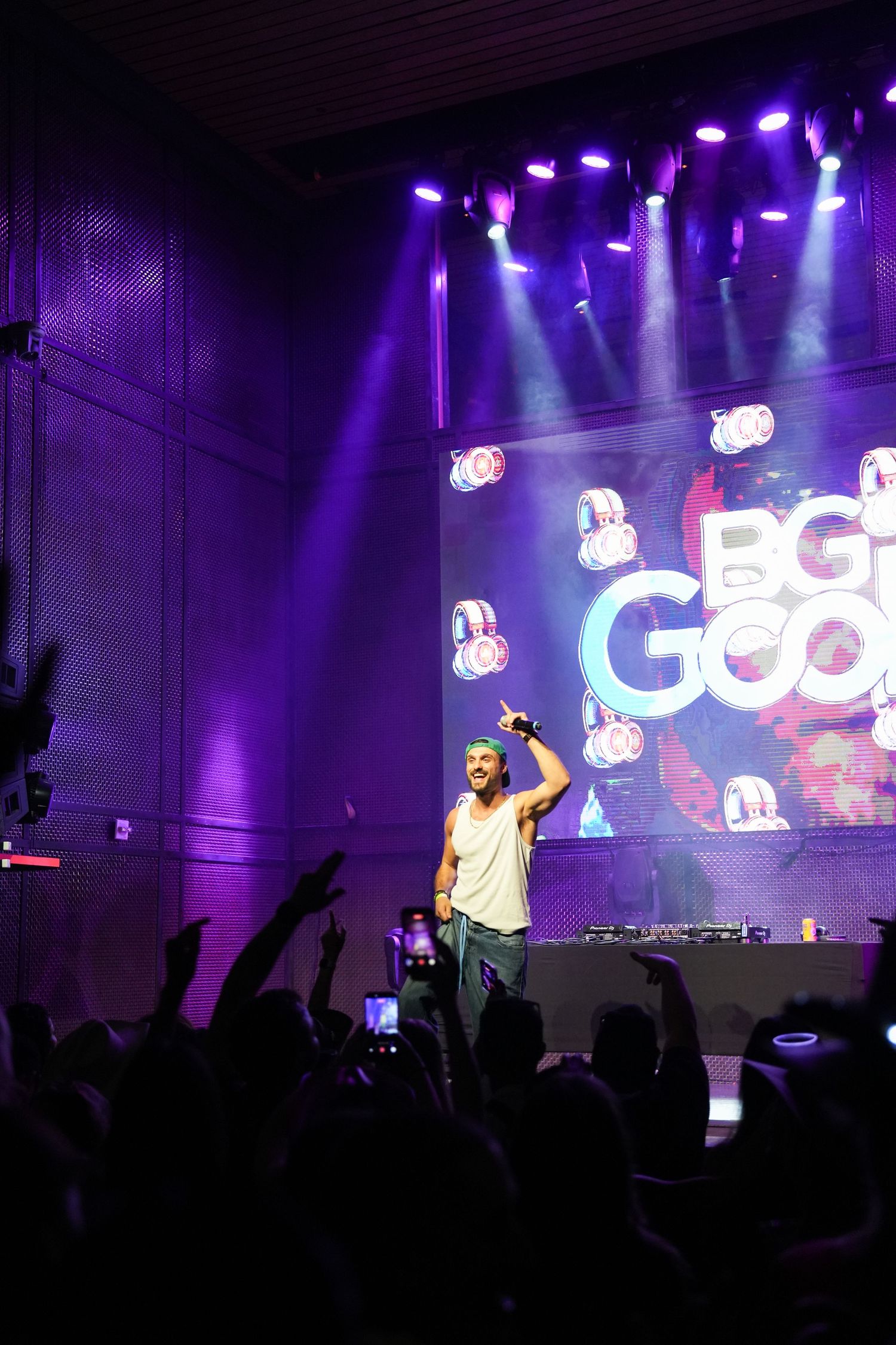 Concert performers on stage with purple lighting and crowd silhouettes during an energetic live music performance.