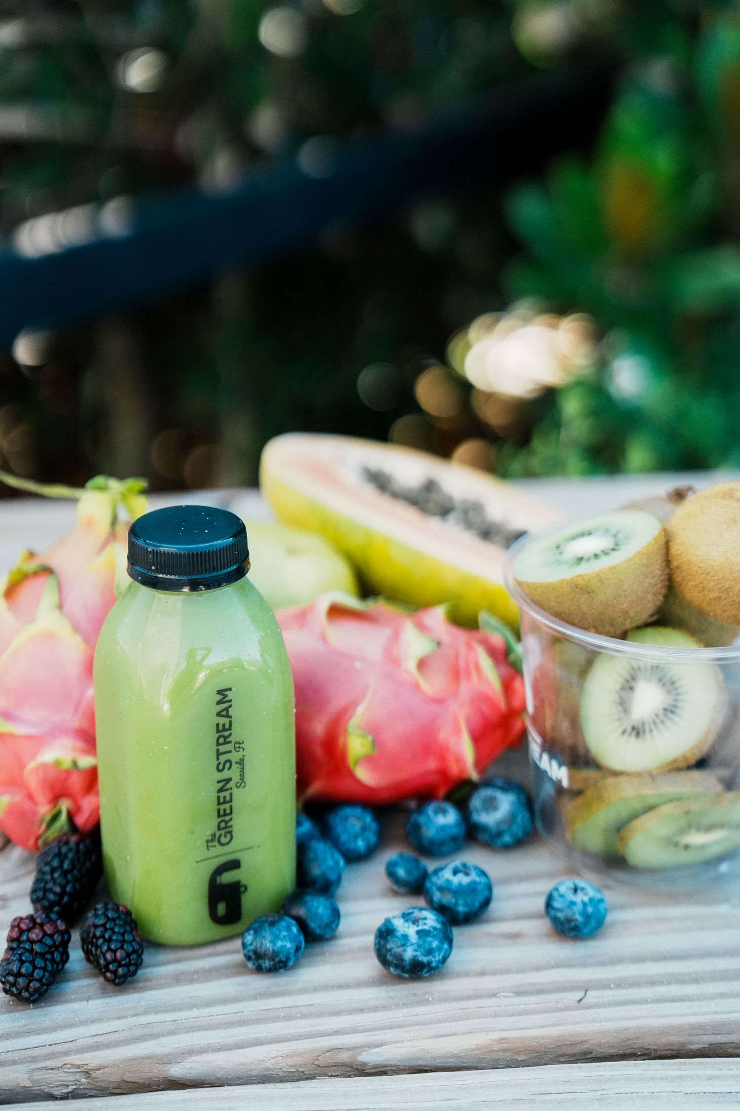 Fresh fruit smoothie ingredients including kiwi, berries and citrus arranged on rustic wooden surface with glass bottles.
