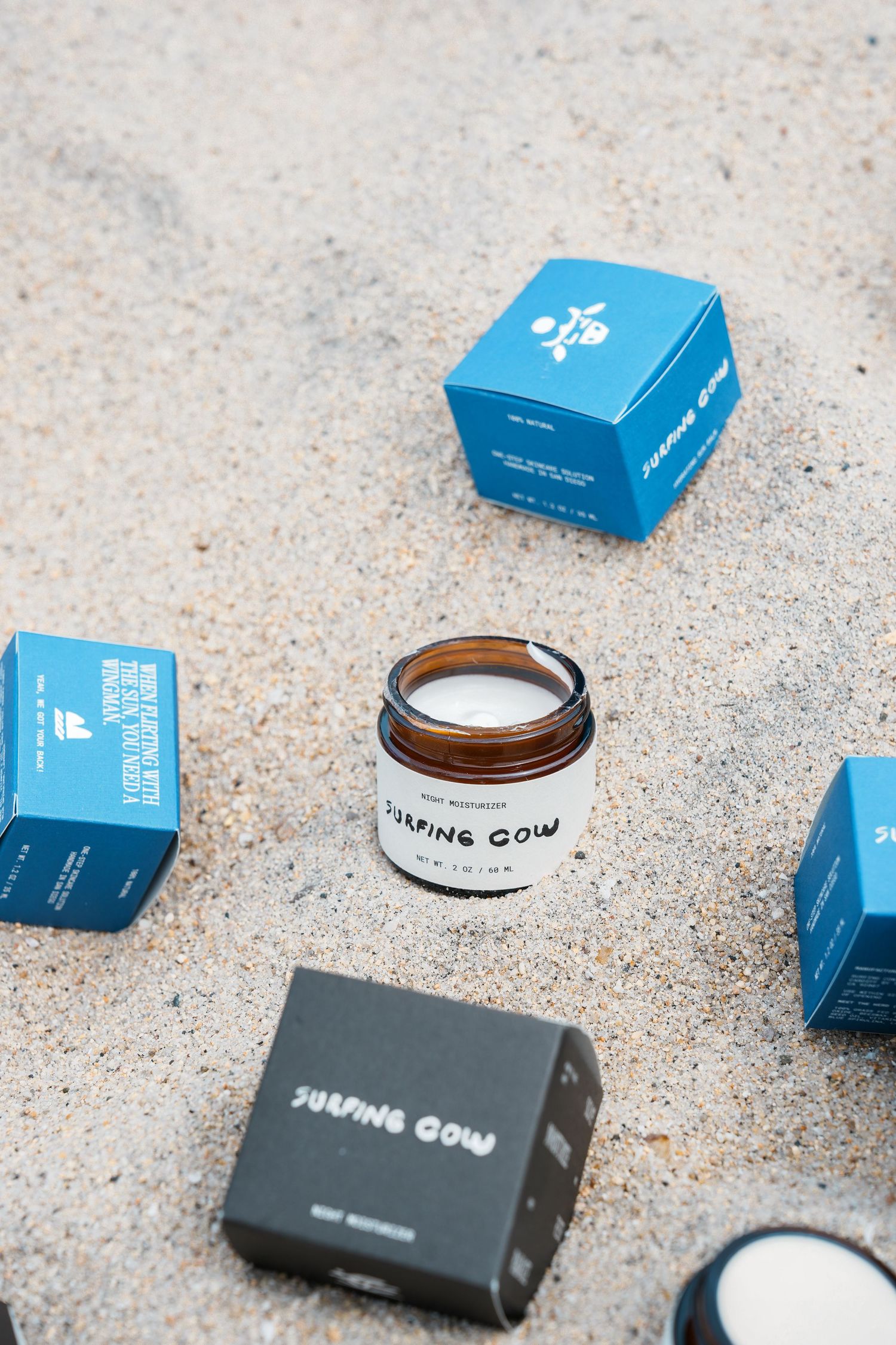 Blue product boxes and containers arranged on a sandy surface showing minimalist packaging design.