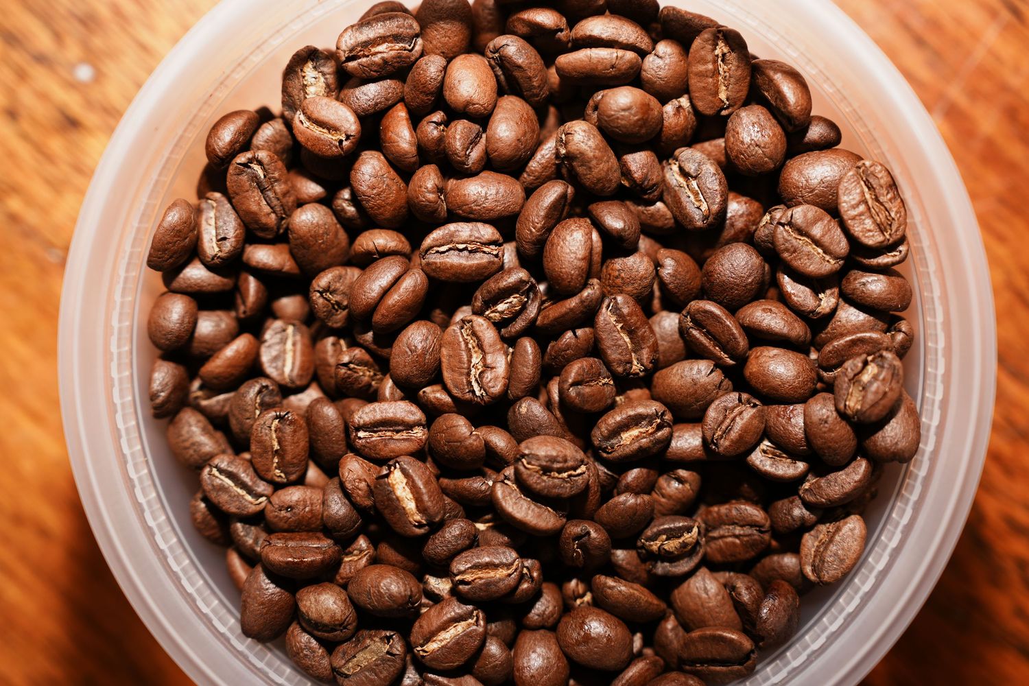 Fresh roasted coffee beans in clear glass containers against a warm wooden background.