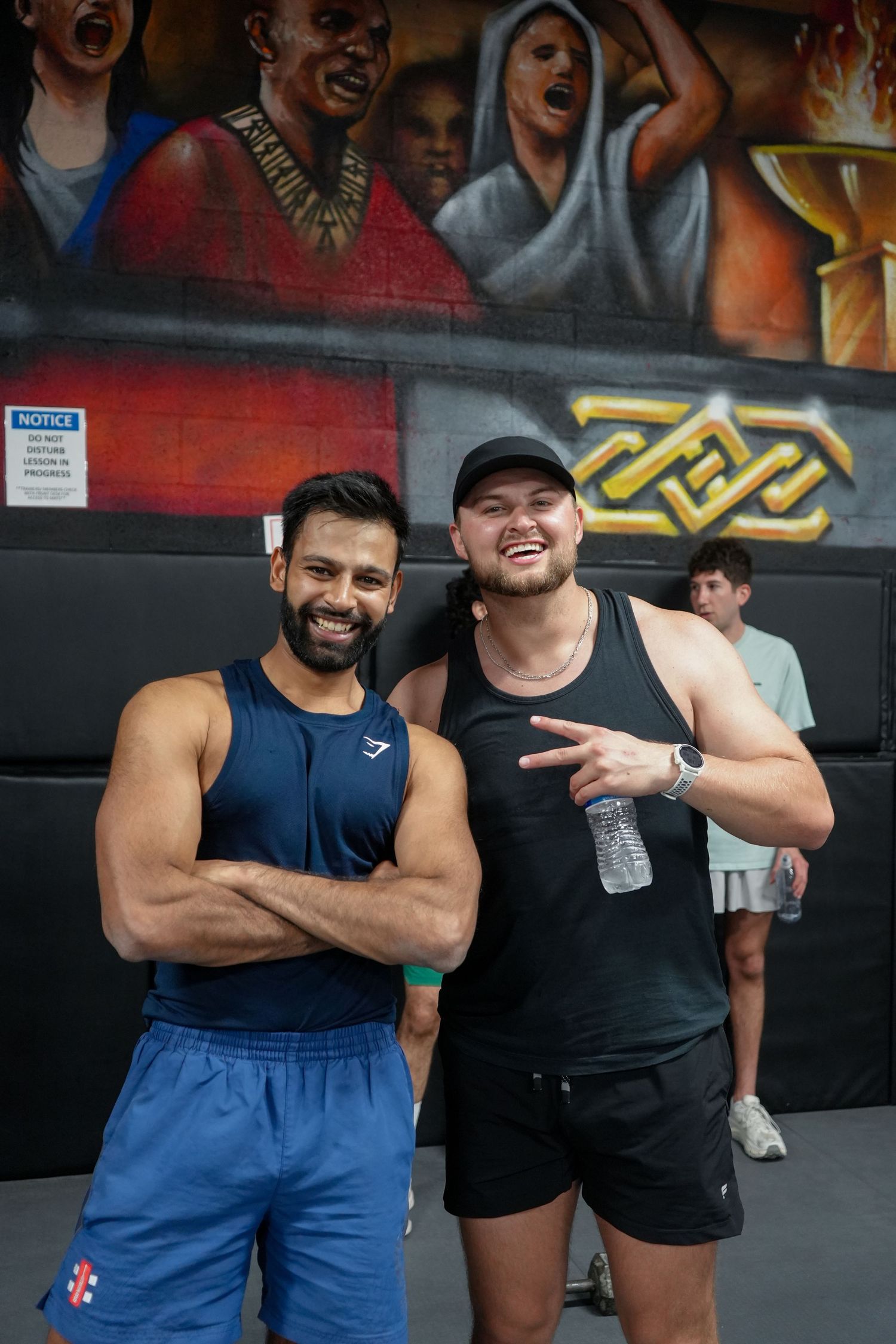 Two people posing together at a fitness center with colorful graffiti wall in background.
