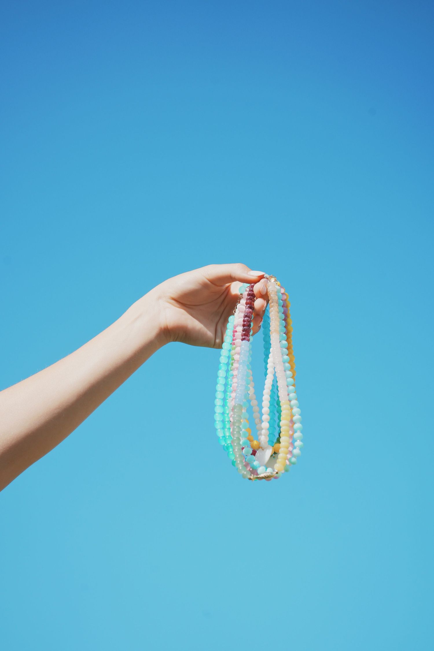 Hand holding colorful beaded necklaces against bright blue sky background.