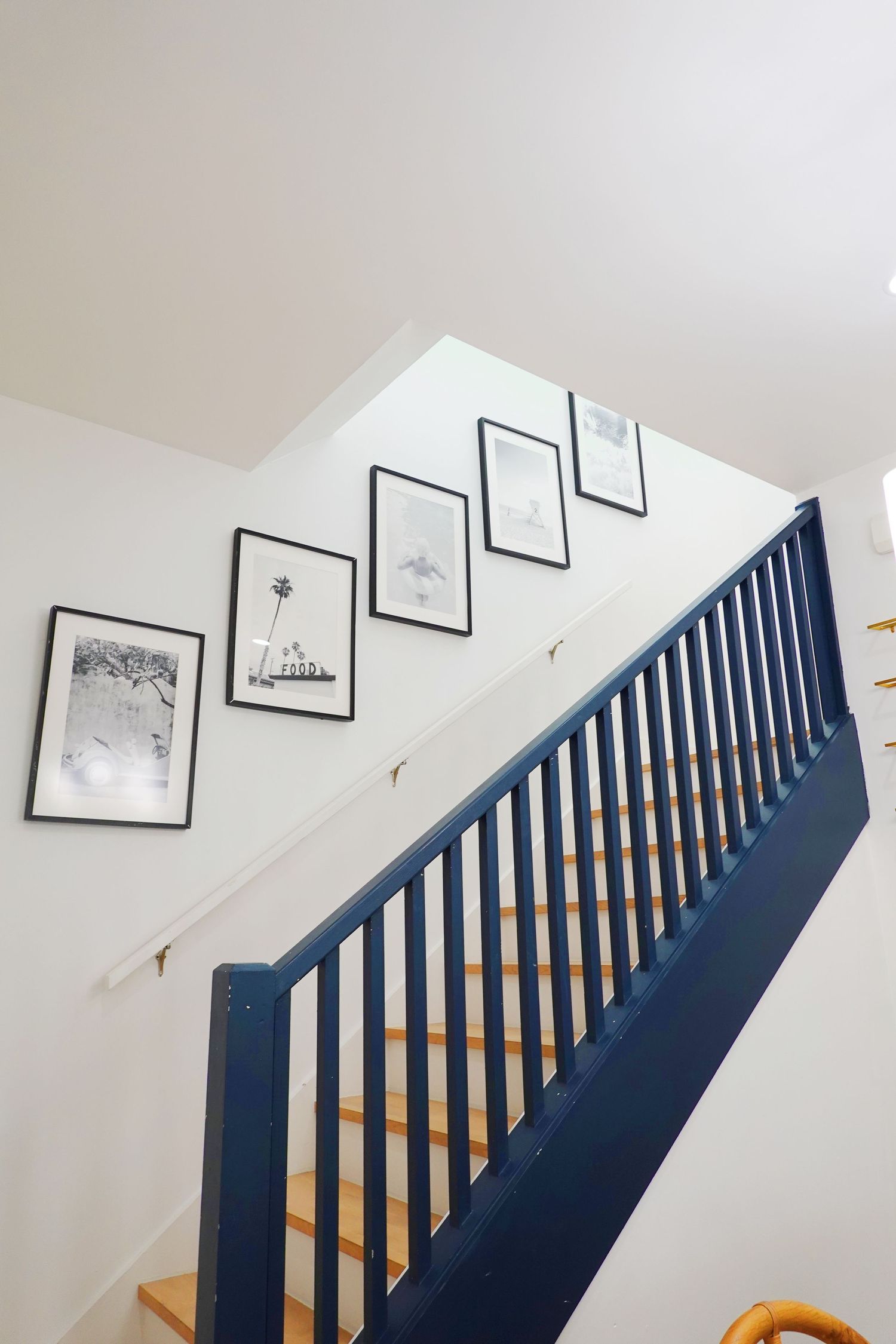 Navy blue staircase railing with black and white framed artwork arranged along white wall.