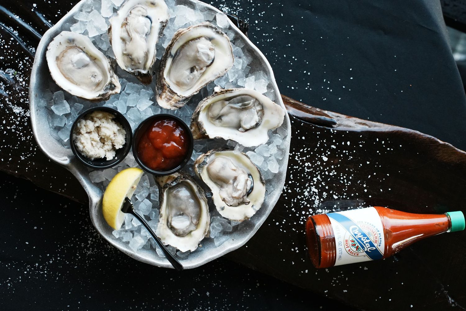 Fresh oysters on ice with lemon wedges and cocktail sauce served alongside a cold beer in a restaurant setting.