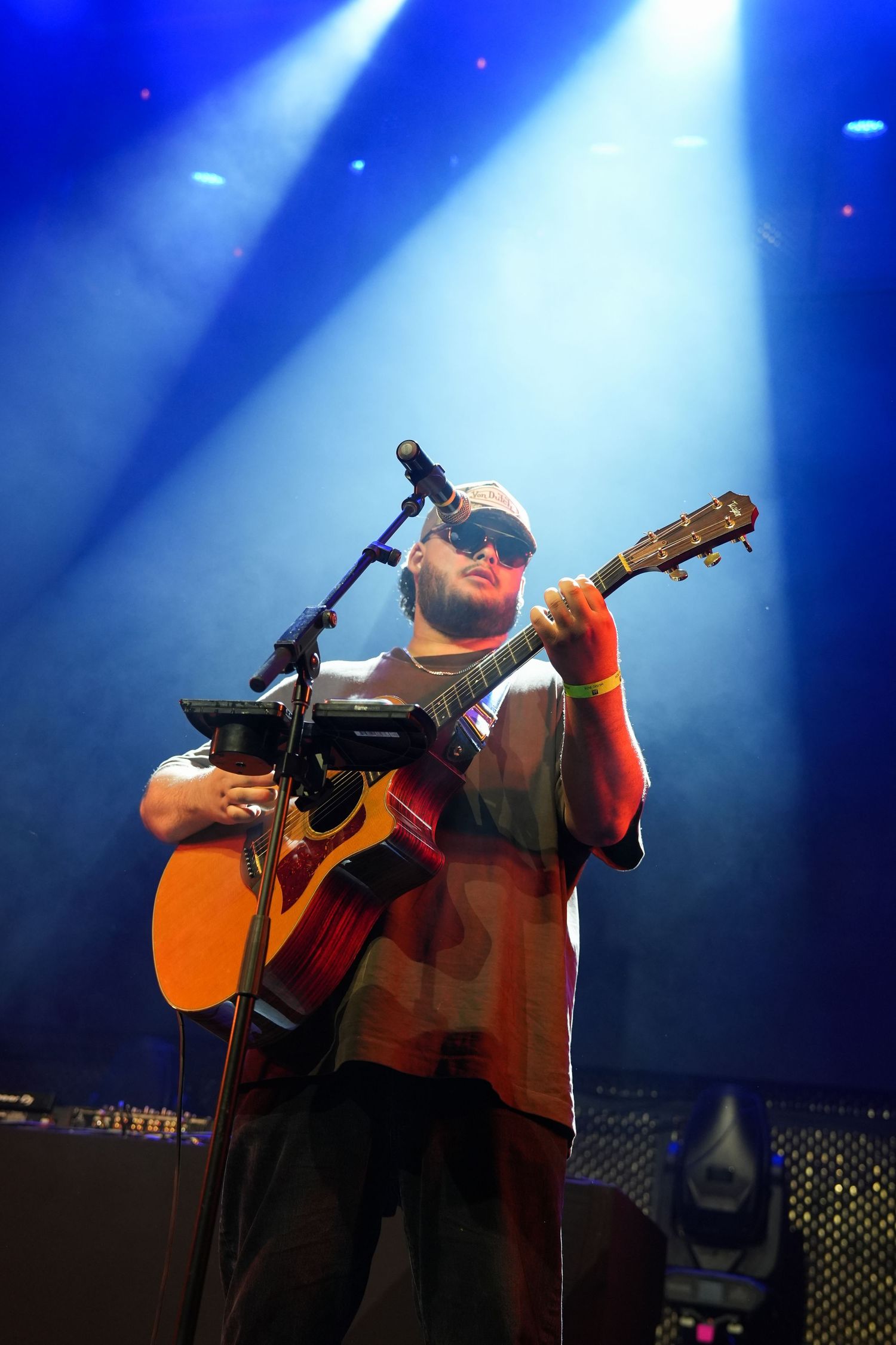 A musician performs on stage under dramatic blue lighting with an acoustic guitar at a live concert venue.