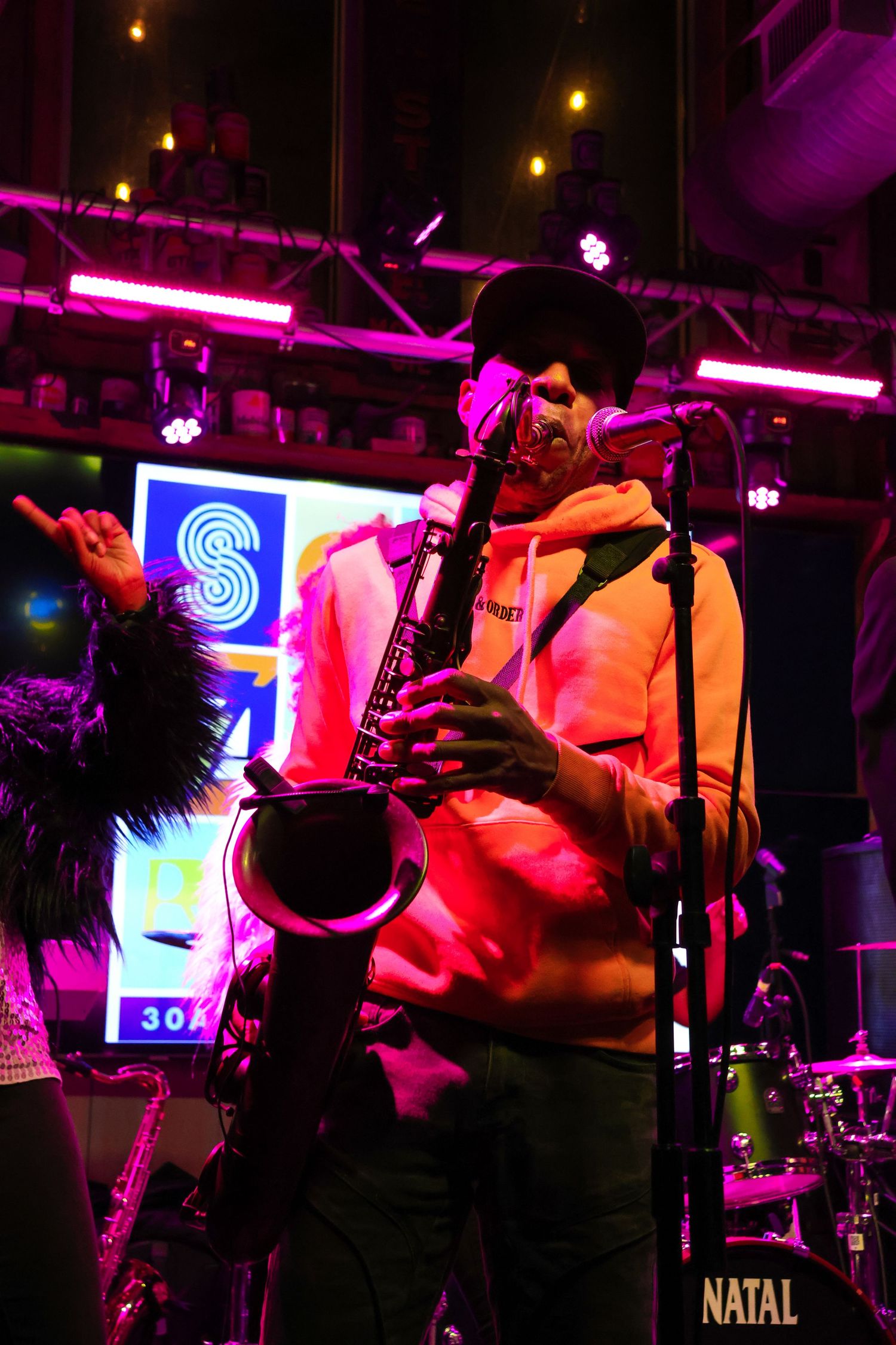 Saxophone player performing under pink and purple stage lighting with neon signage.