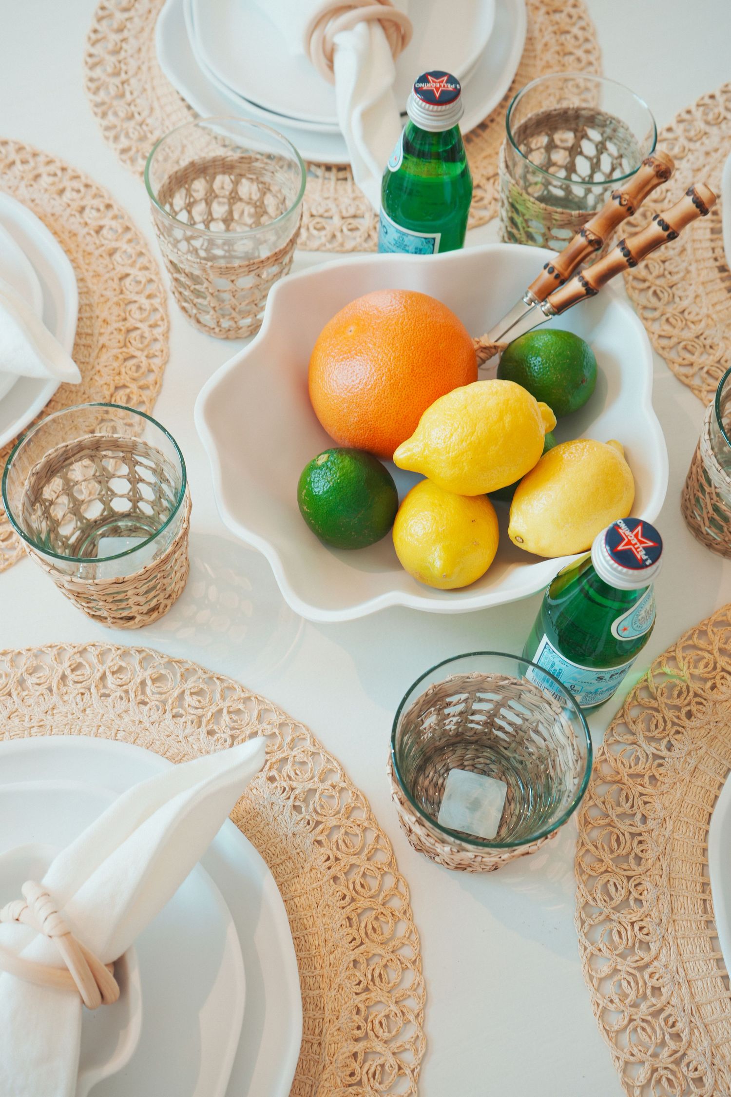 Vintage crystal glassware and citrus fruits arranged on white lace tablecloth with mineral water bottles and napkins.