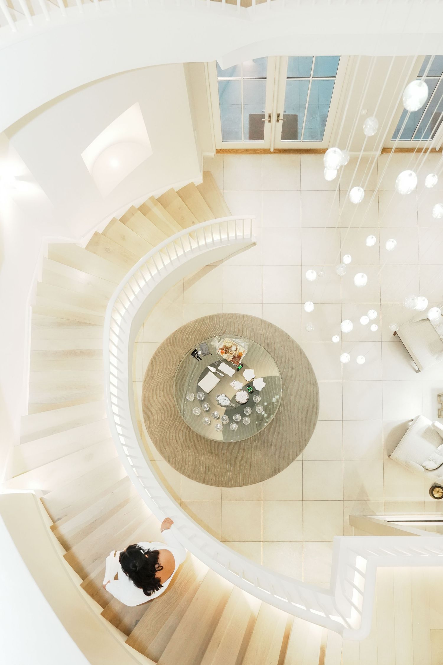 Spiral staircase in modern white interior with circular design and pendant lights.