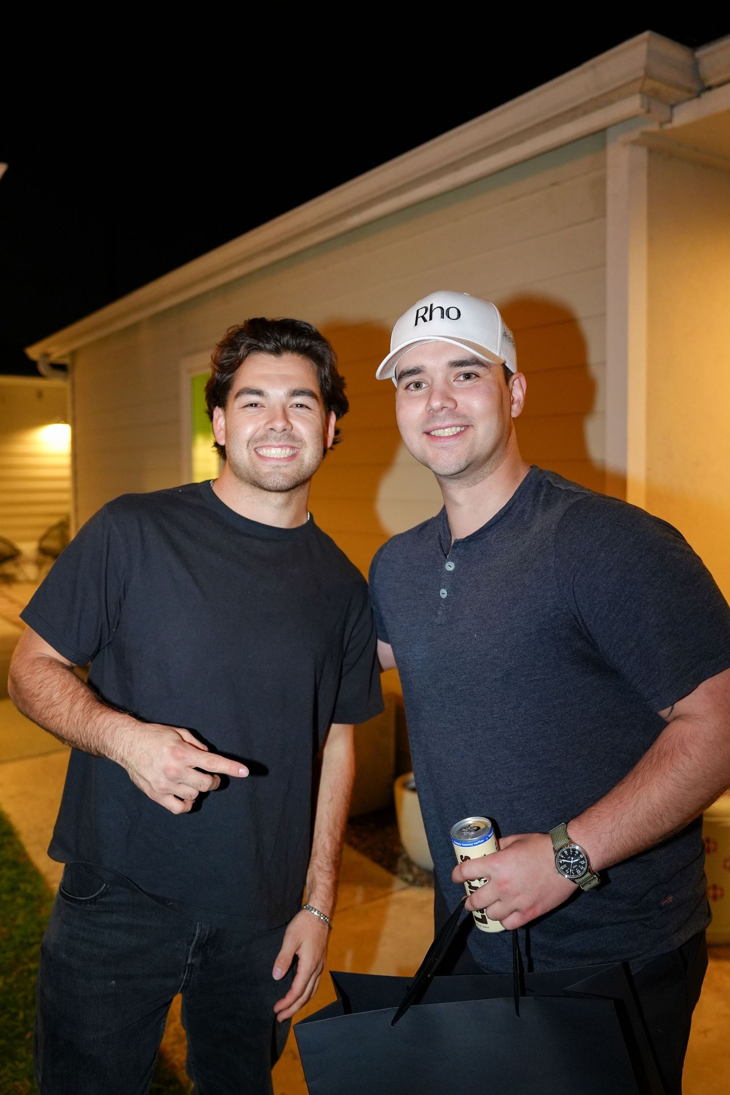 Two people wearing dark shirts stand together smiling and posing for casual outdoor photos at night.