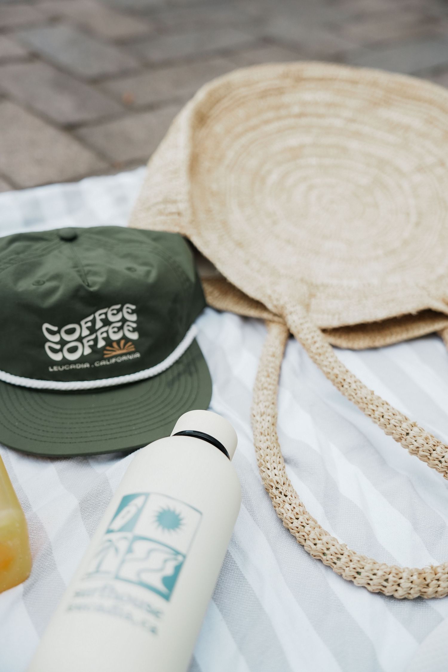 Green bucket hat with coffee branding lies on white surface next to woven straw accessories.