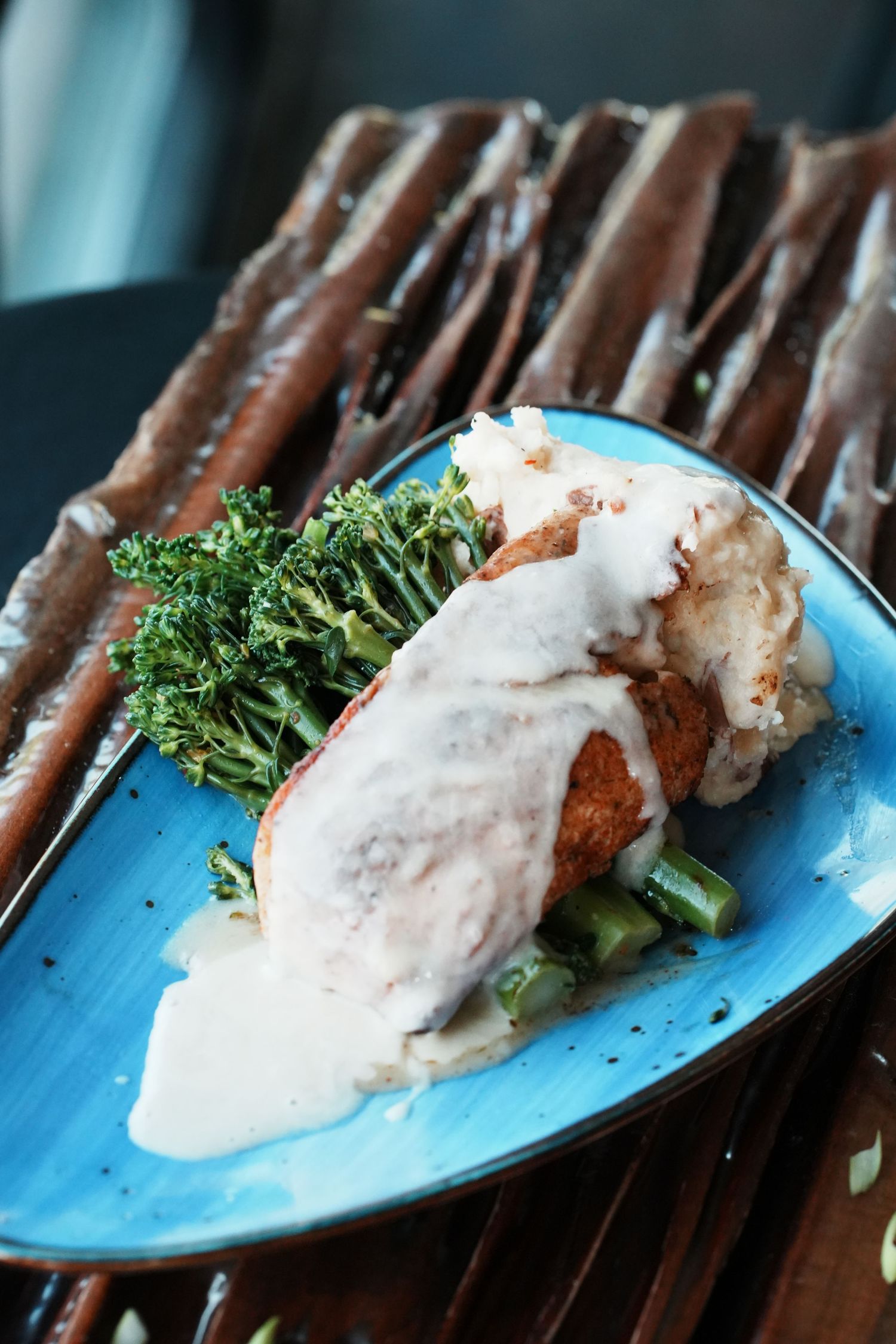 Grilled chicken cutlet covered in cream sauce served with sautéed broccolini on a bright blue plate.