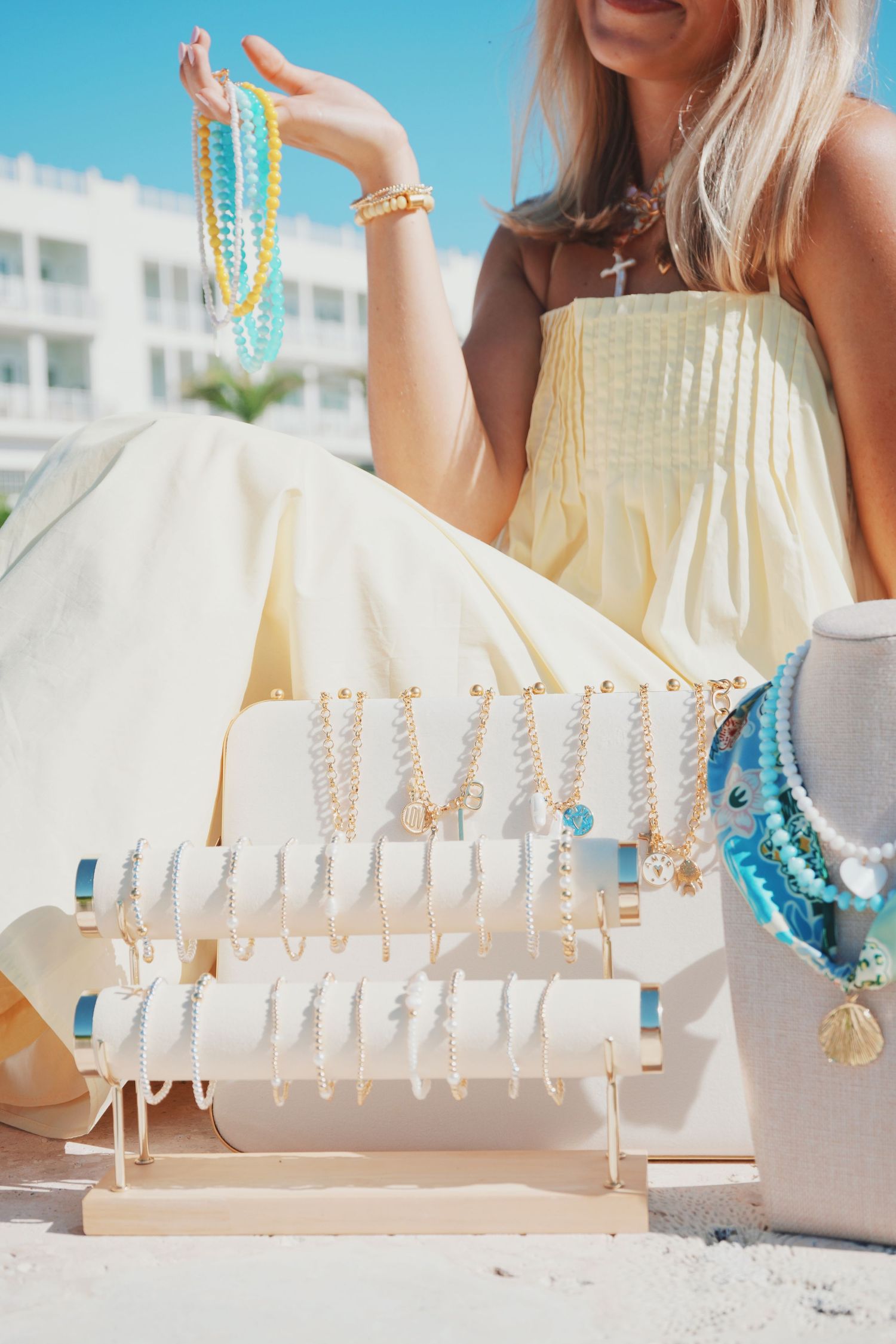White seashell necklaces displayed on a white rack at a beach market with turquoise beaded jewelry accents.