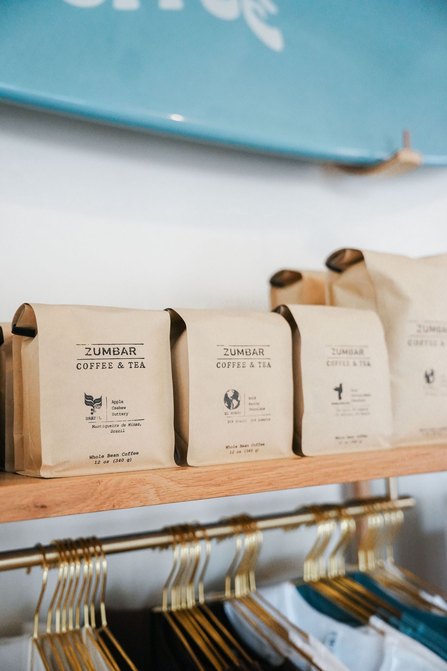 Rows of Junmar coffee and tea bags displayed on wooden shelving in a retail setting.