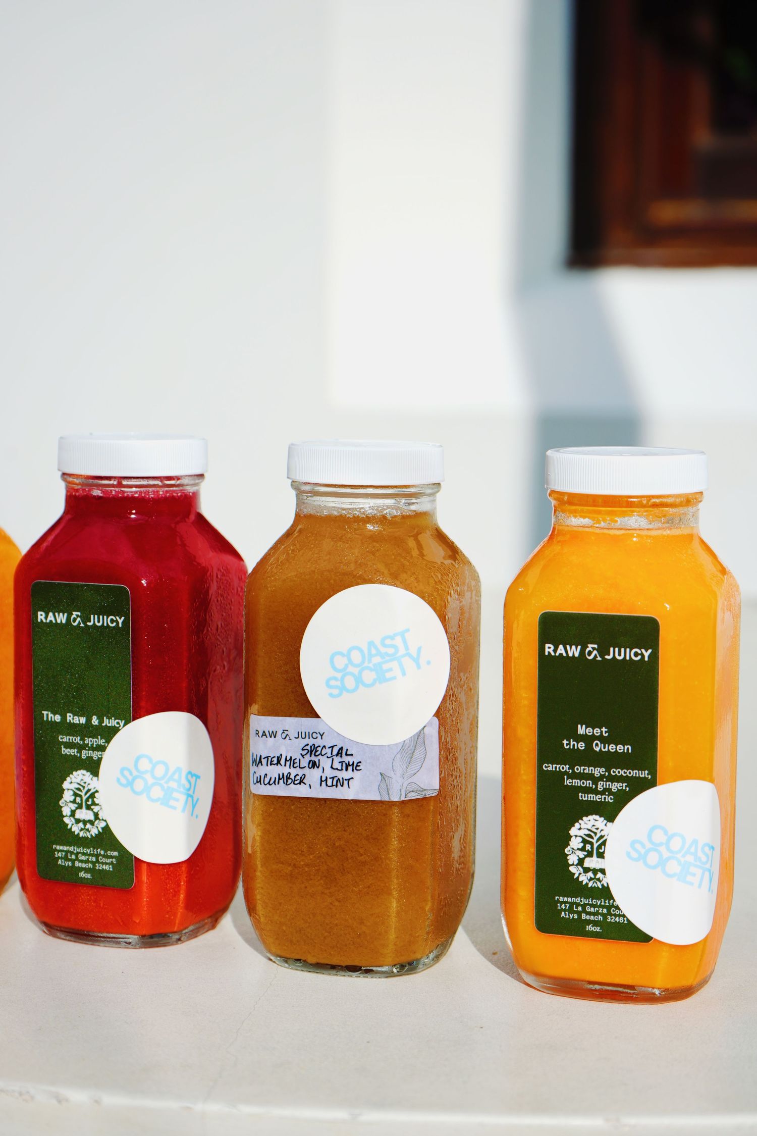 A row of colorful juice bottles with various labels displayed on a white shelf shows different raw and fresh juice varieties.