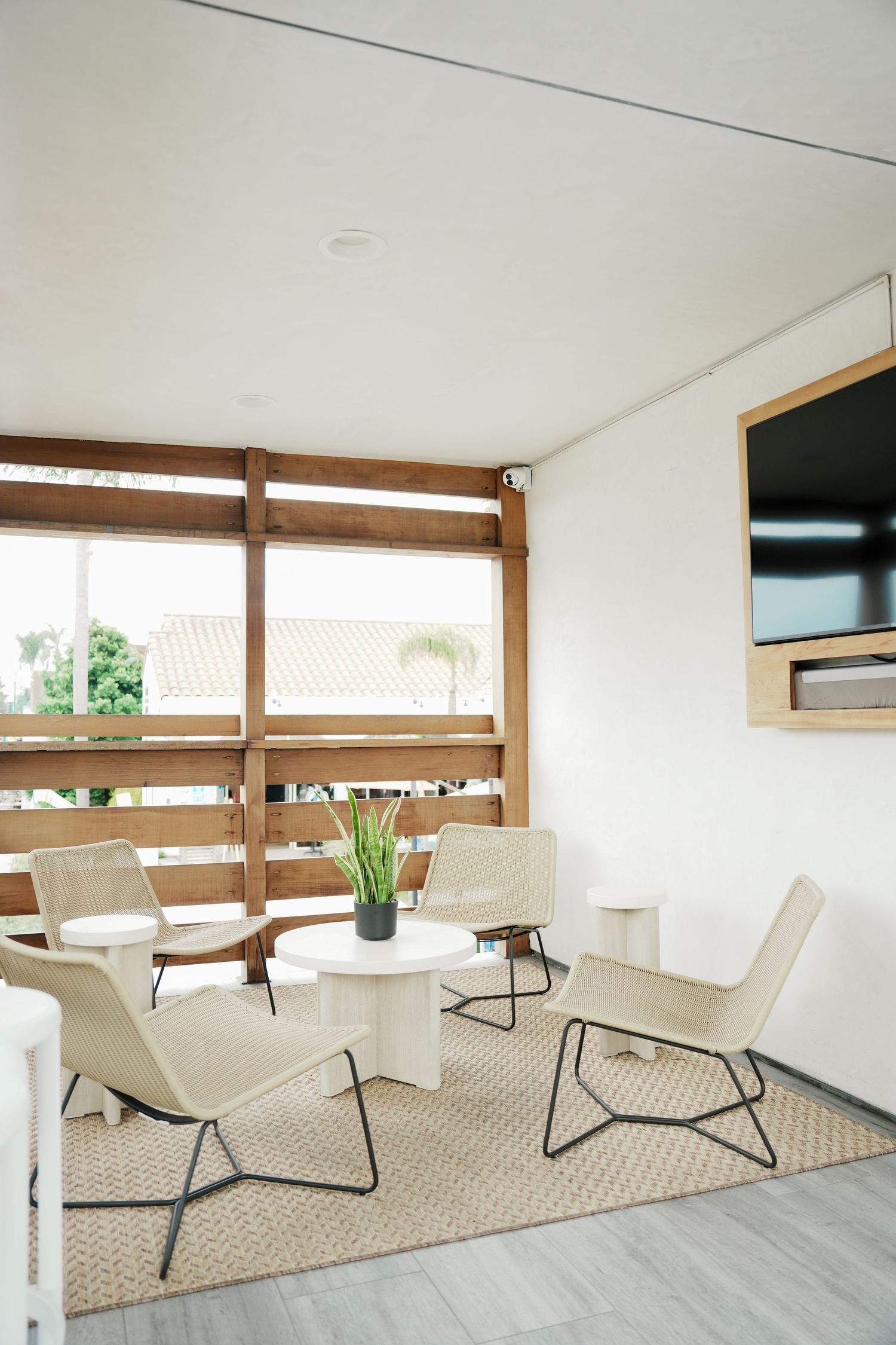 Modern minimalist living space with white lounge chairs, wooden slatted wall, and mounted TV in a bright interior setting.