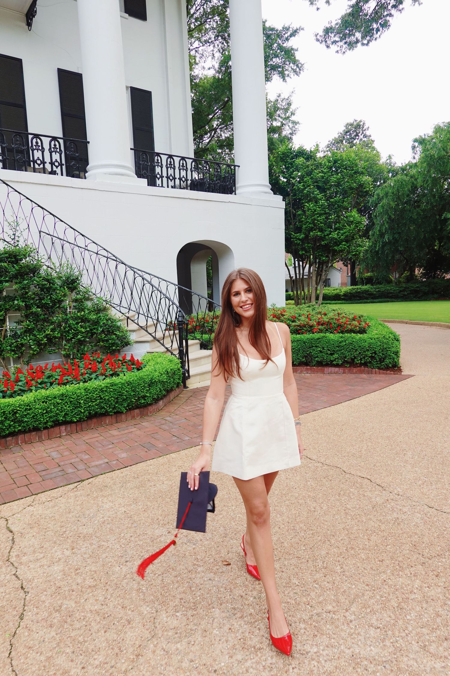Elegant white dress photo at a southern style mansion with red heels and brick walkway.