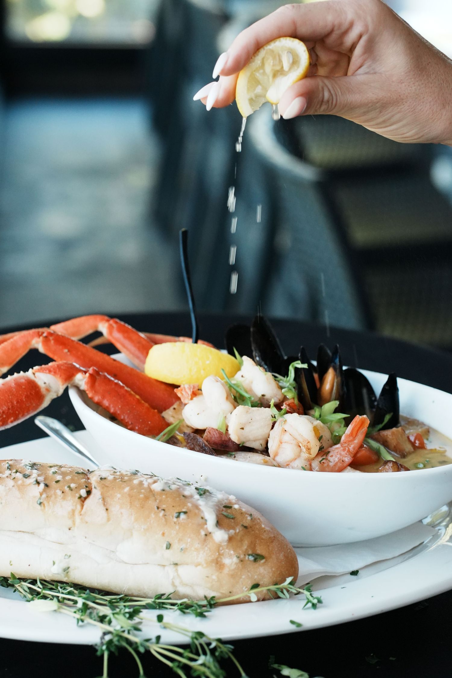 Fresh seafood platter with crab legs and shrimp being drizzled with lemon juice alongside crusty bread and herbs.